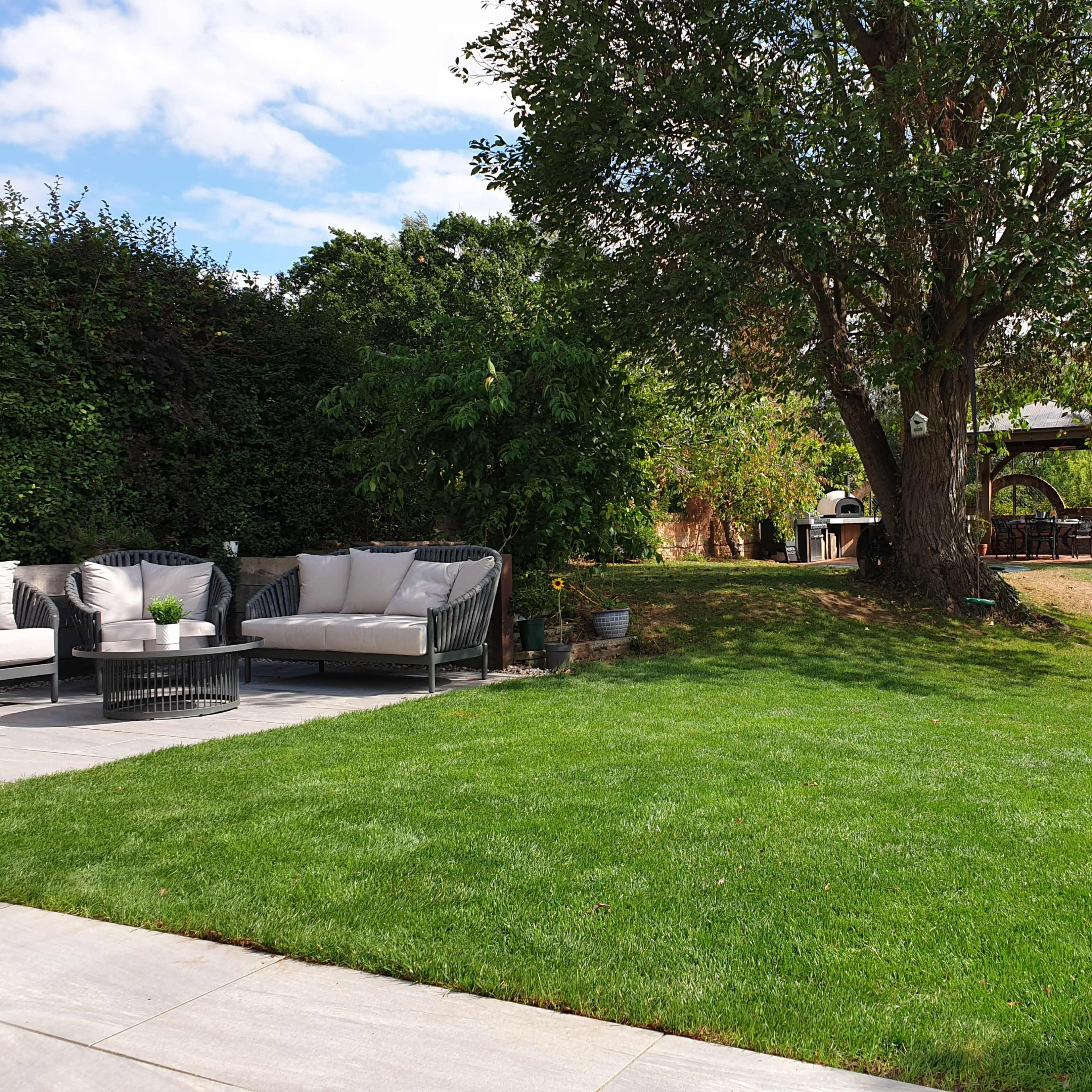 The scene depicts a grassy backyard with a seating area, a tree, and a small playhouse in the background.