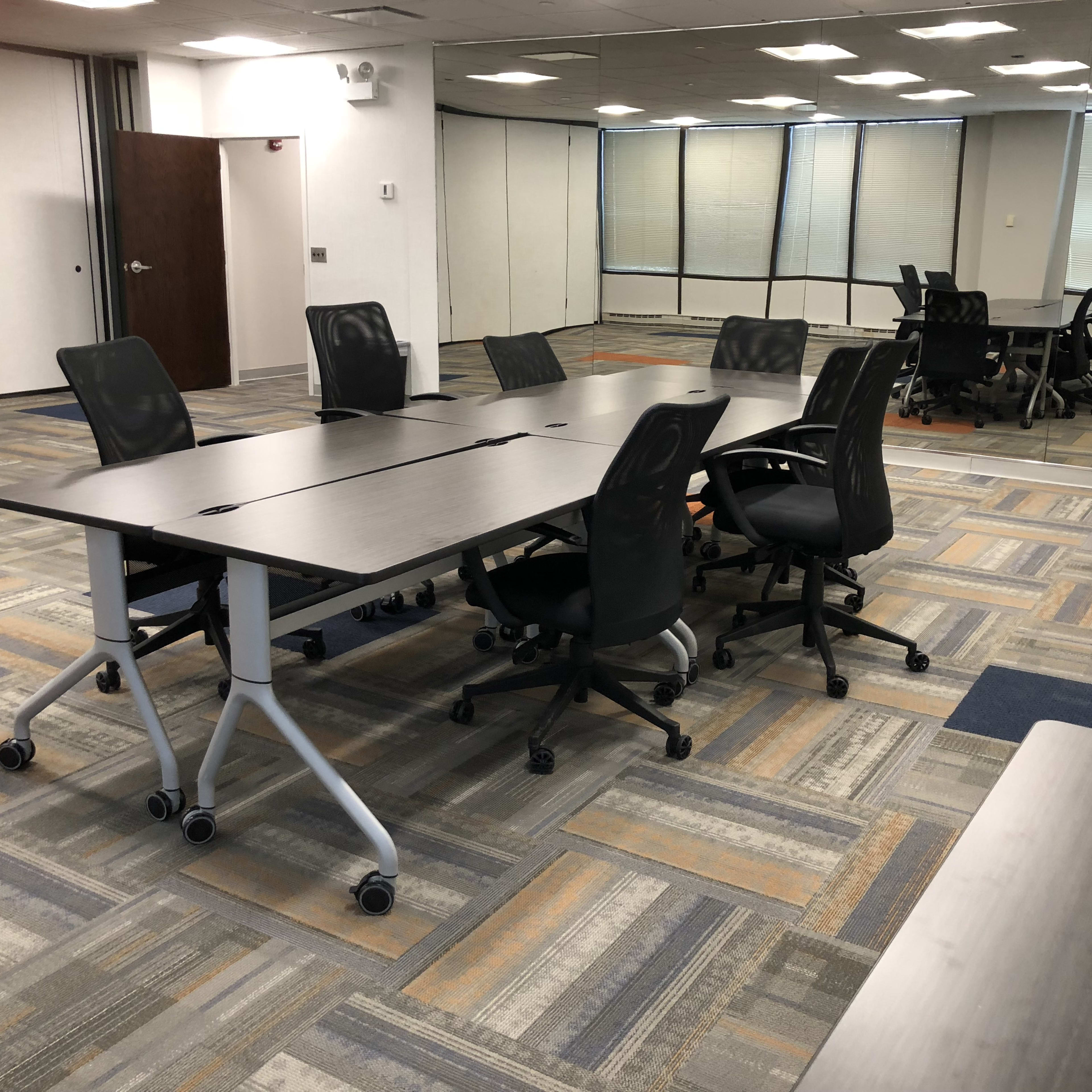A modern office space with several movable desks and rolling chairs arranged on a patterned carpet.