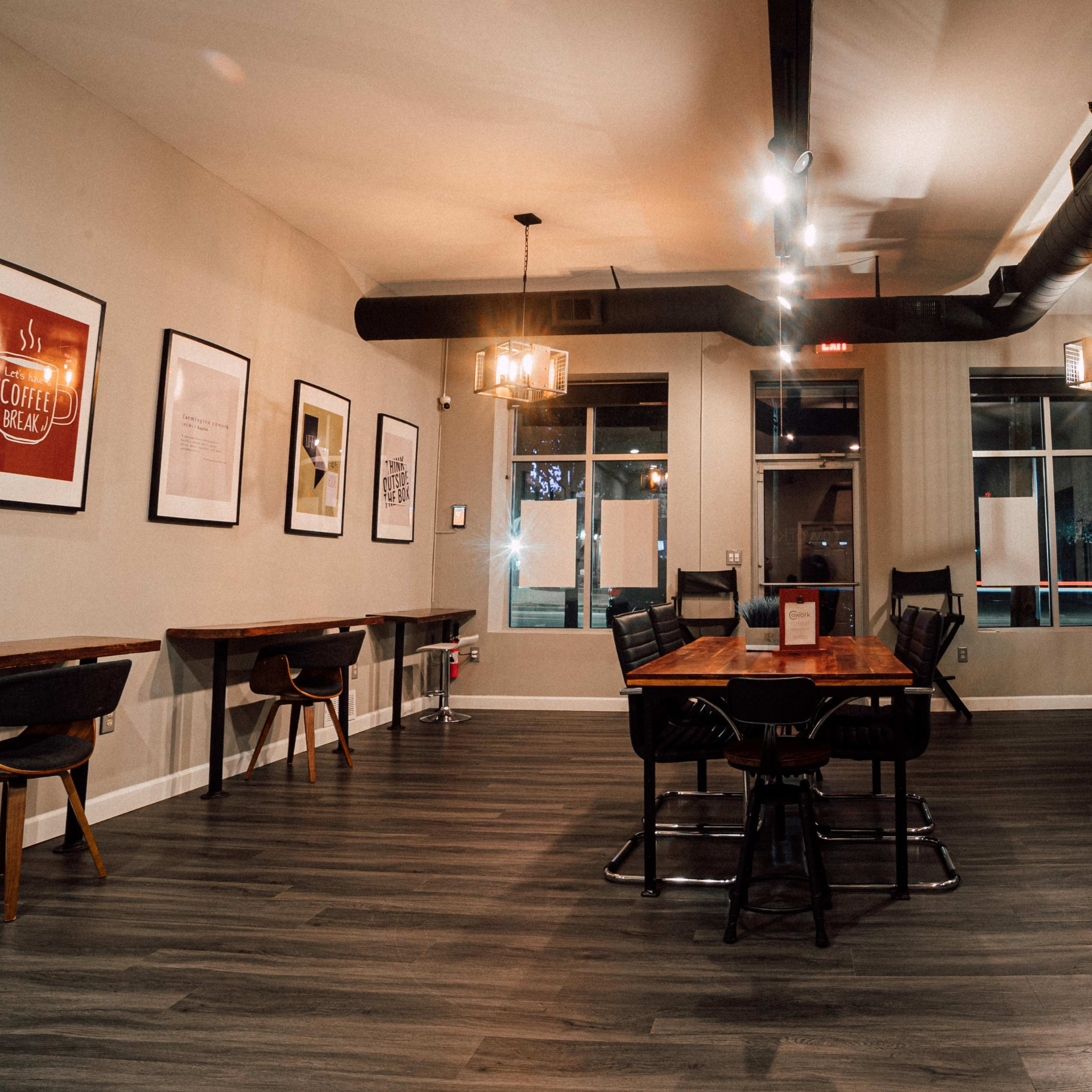 A spacious, modern cafe interior with wooden tables, black chairs, and framed artwork on the walls.