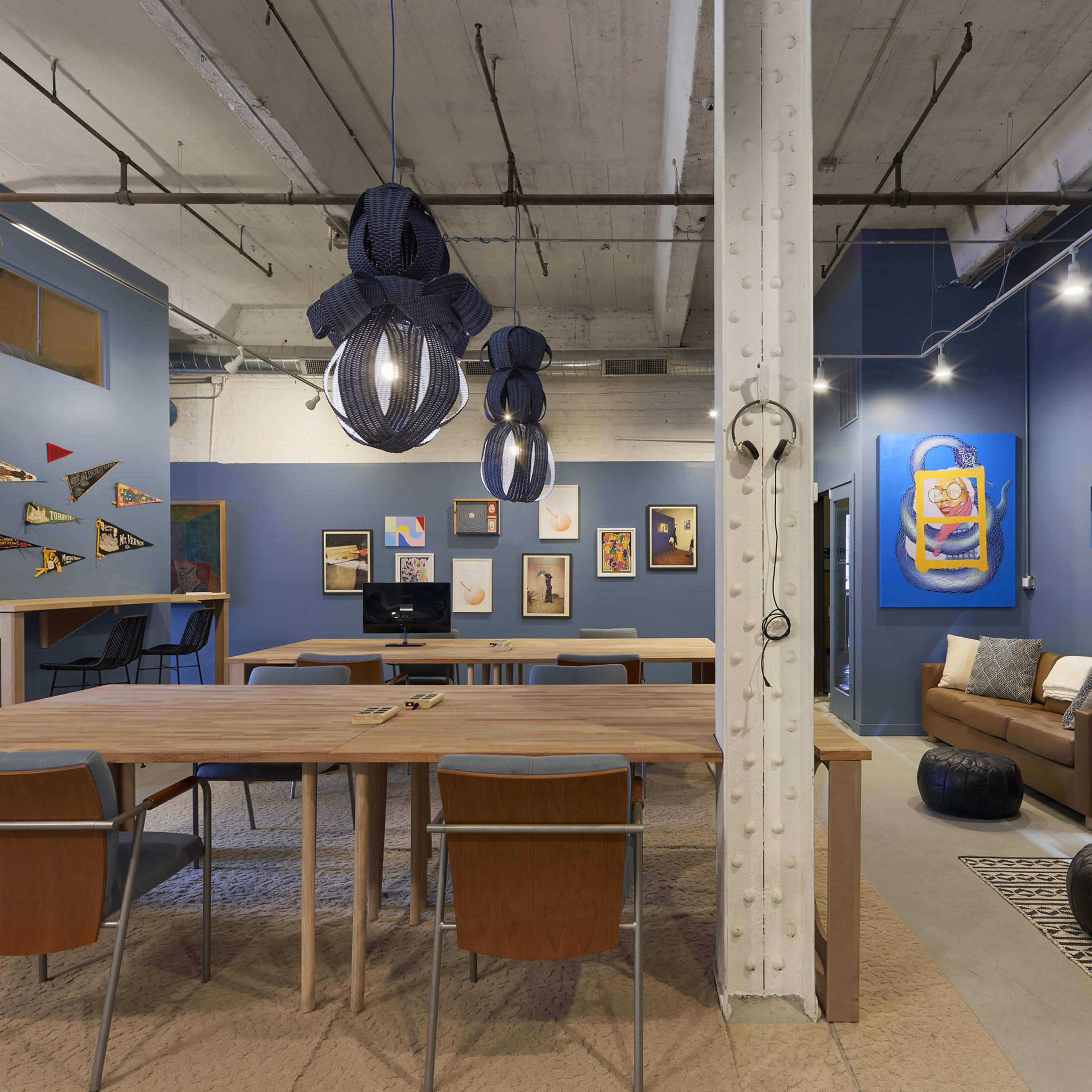 A spacious open-plan office featuring wooden tables, modern pendant lighting, and colorful wall art.