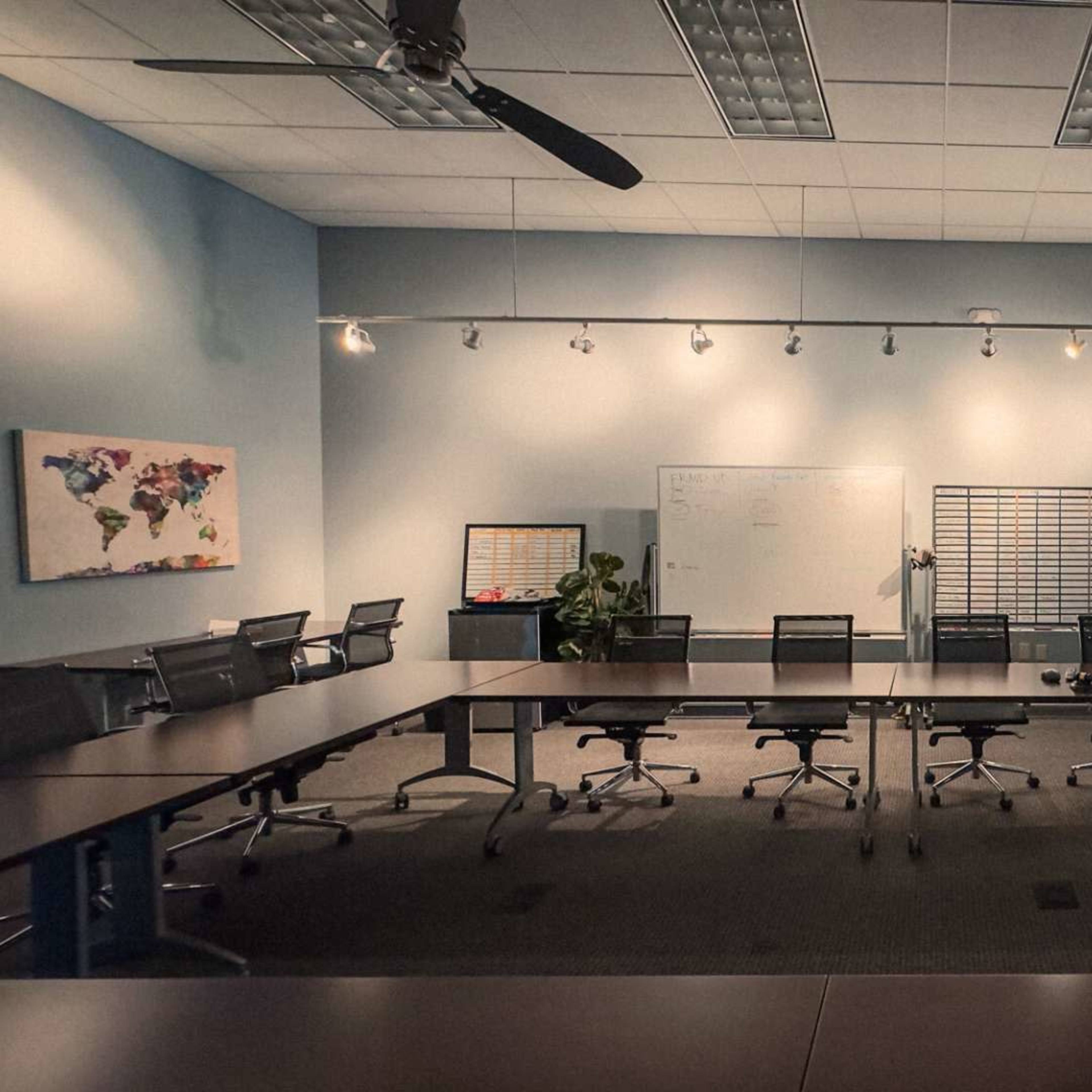 A well-lit conference room features a large table surrounded by black office chairs, a whiteboard, and a world map on the wall.
