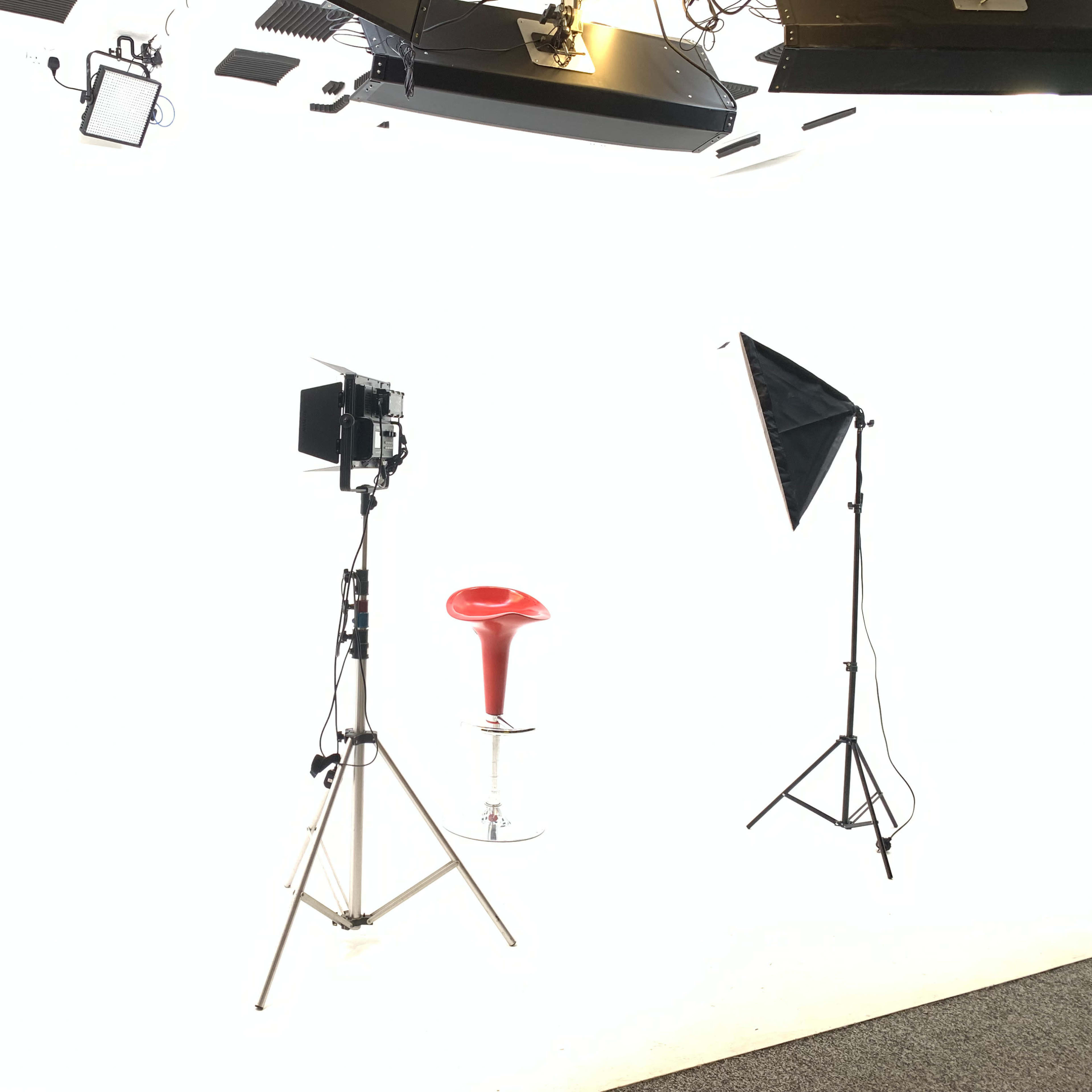 A red bar stool is positioned in a brightly lit studio setup with two light stands.