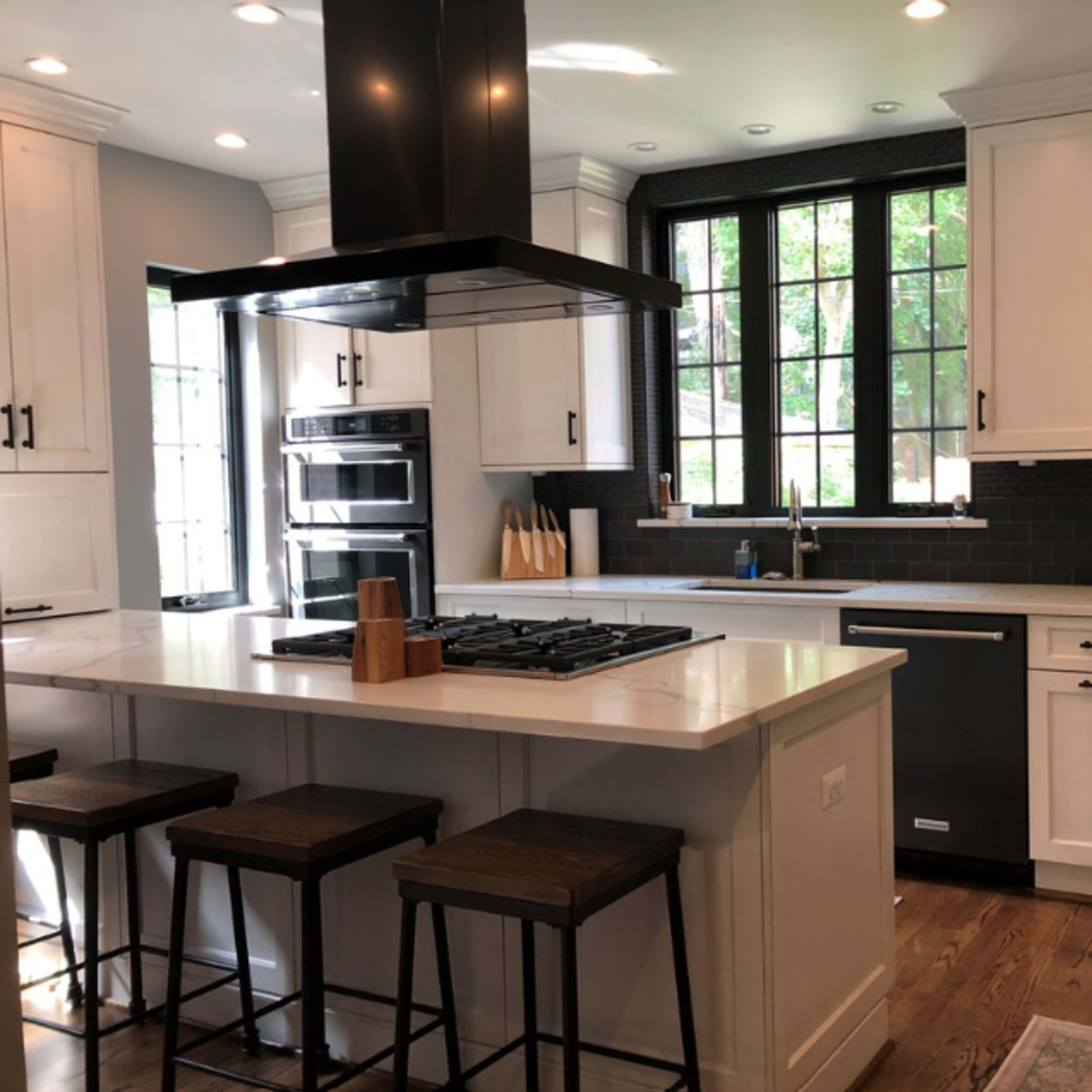 A modern kitchen features a large island with bar stools, a gas cooktop, and a black-and-white color scheme with ample natural light from windows.