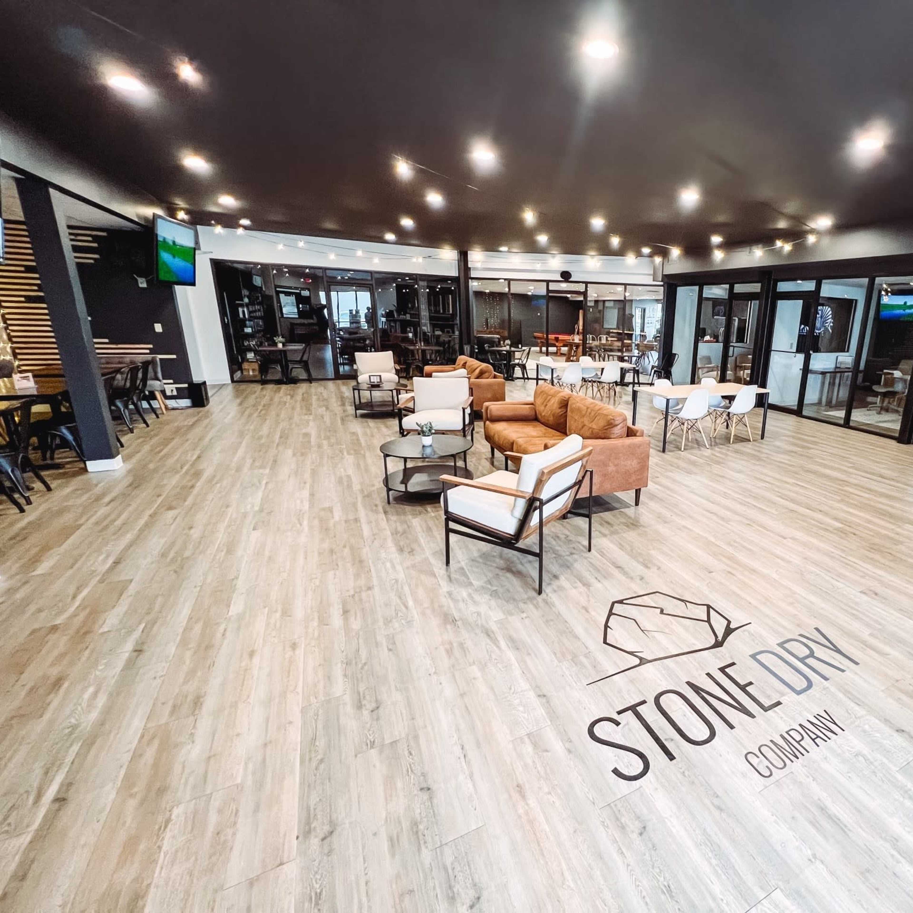 The interior of a modern office space features a seating area with brown armchairs, tables, and a large logo on the floor.