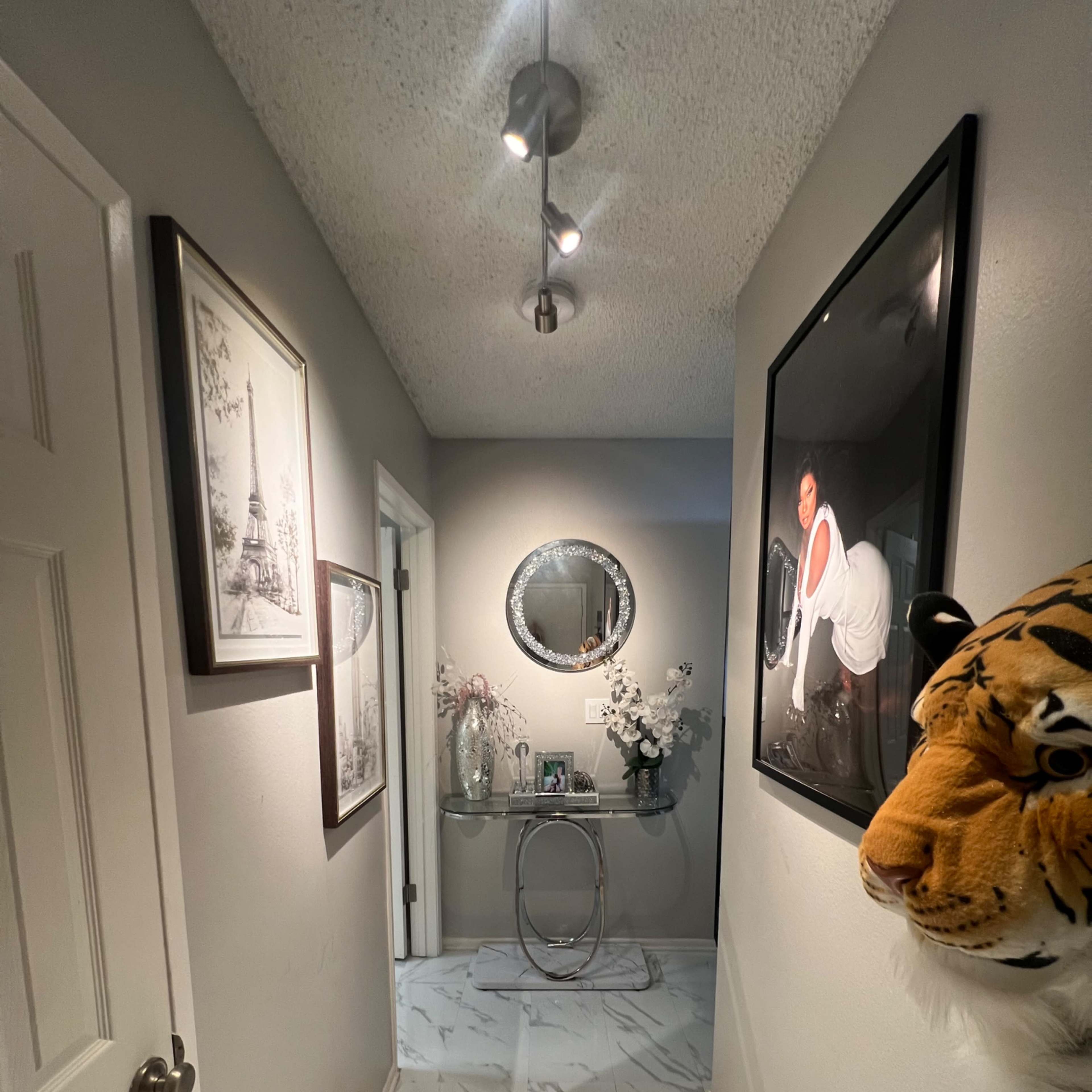 A hallway featuring marble-patterned flooring, decorative wall art, and a round mirror above a console table.