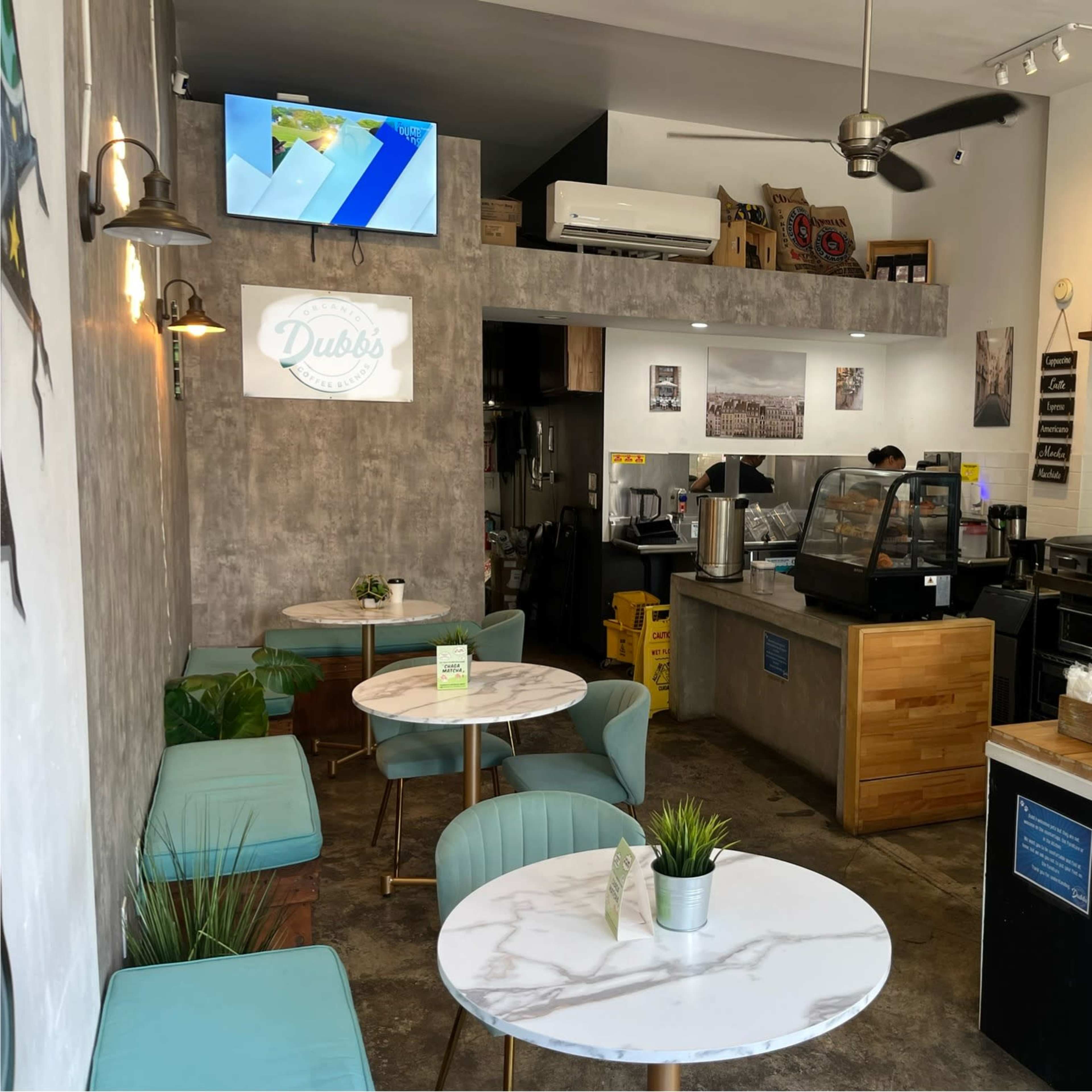 A cozy cafe interior with marble-topped tables, a small counter displaying coffee equipment, and a wall-mounted television.