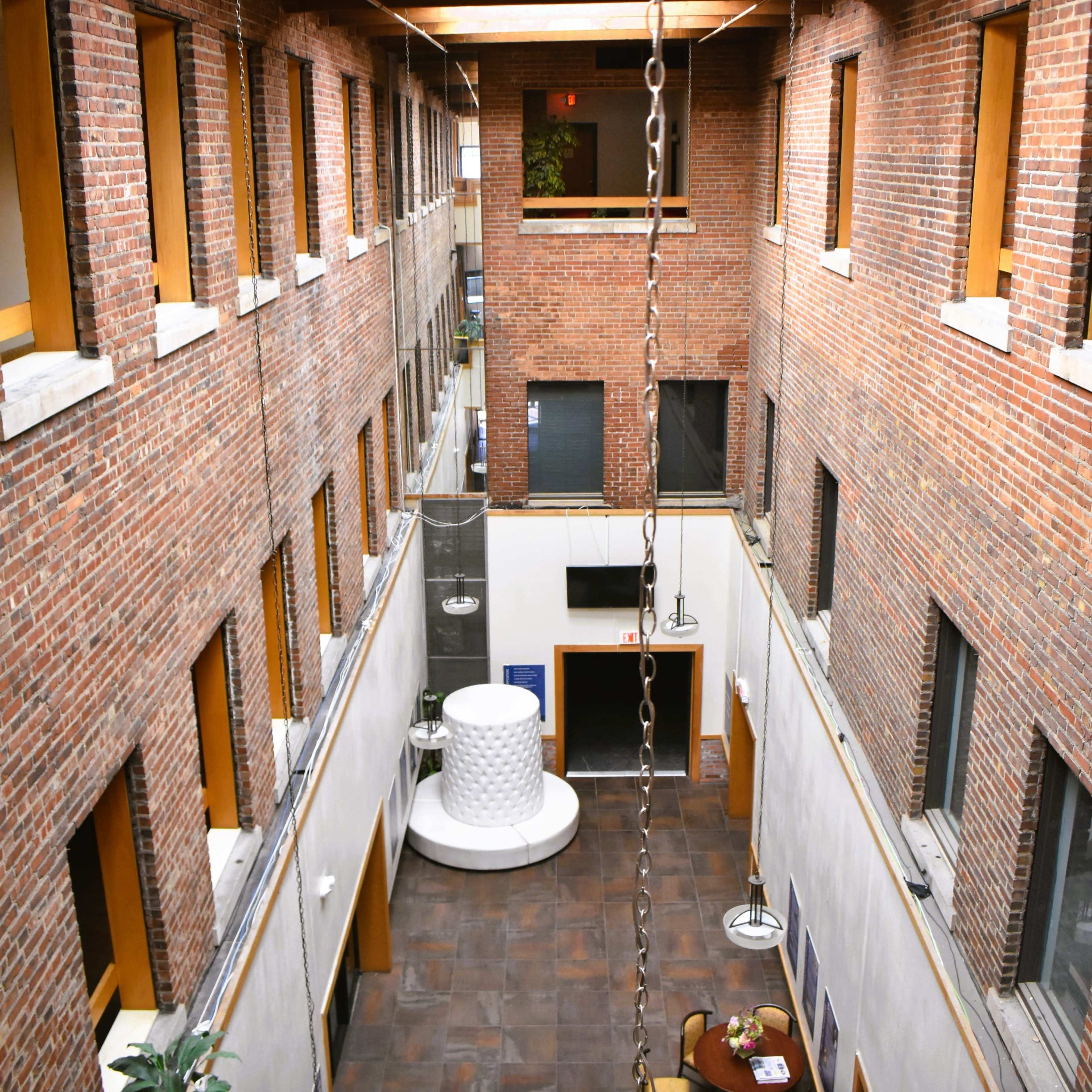 A spacious interior courtyard of a brick building, featuring a round white sculpture and a seating area with a table.