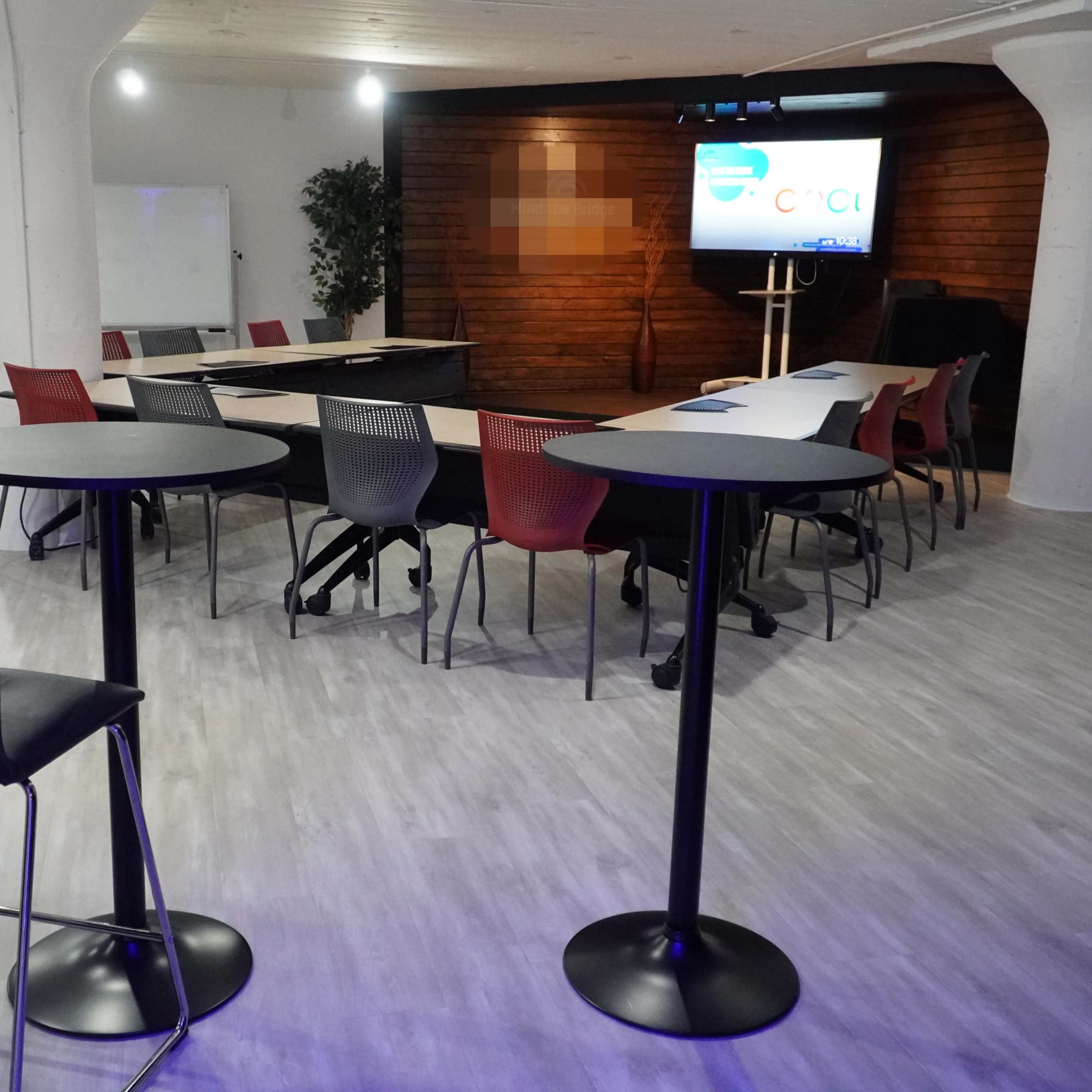 A modern meeting room with a presentation screen, round tables, and chairs arranged for a gathering.