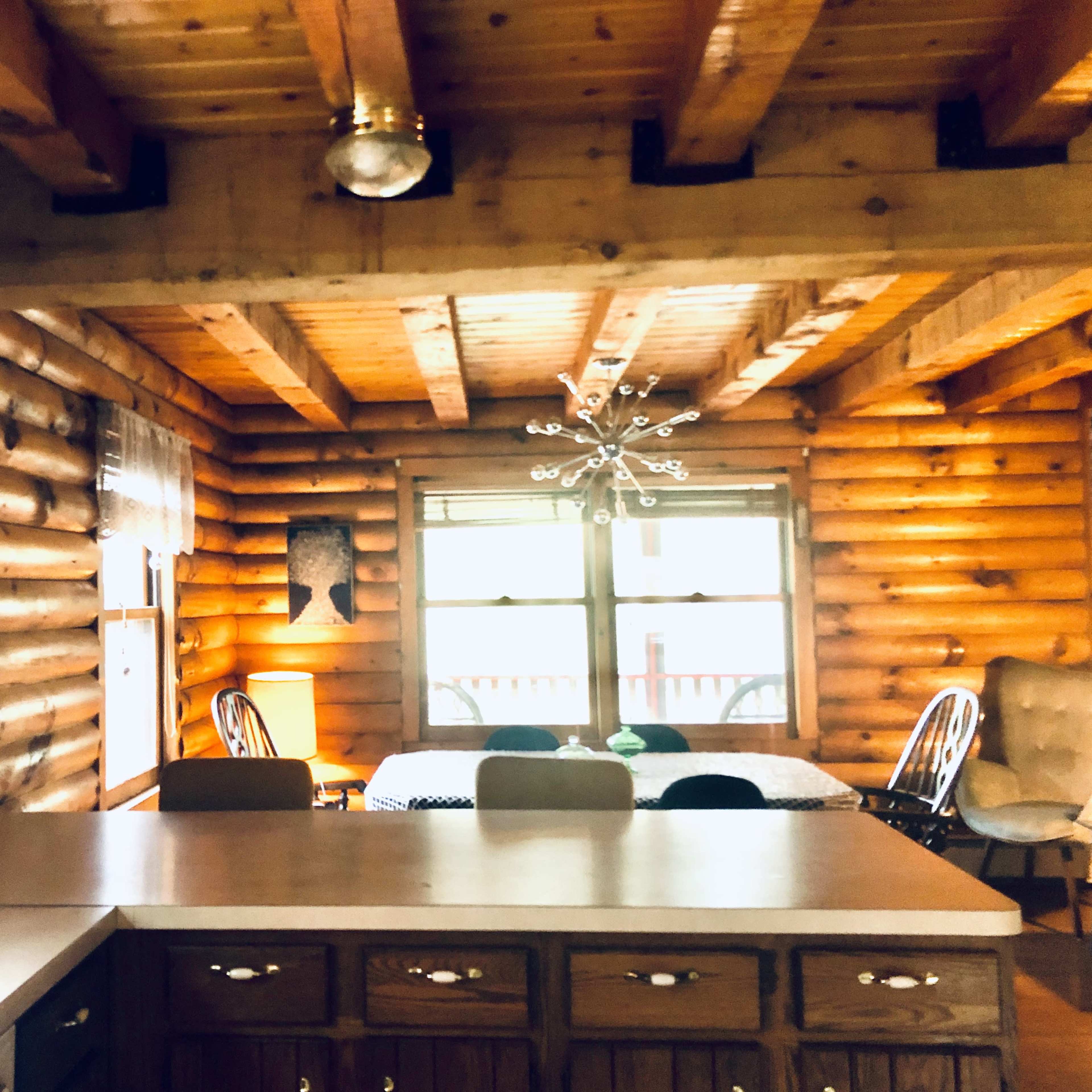 A rustic log cabin interior featuring a kitchen area with wooden cabinetry and a dining area illuminated by a modern chandelier.