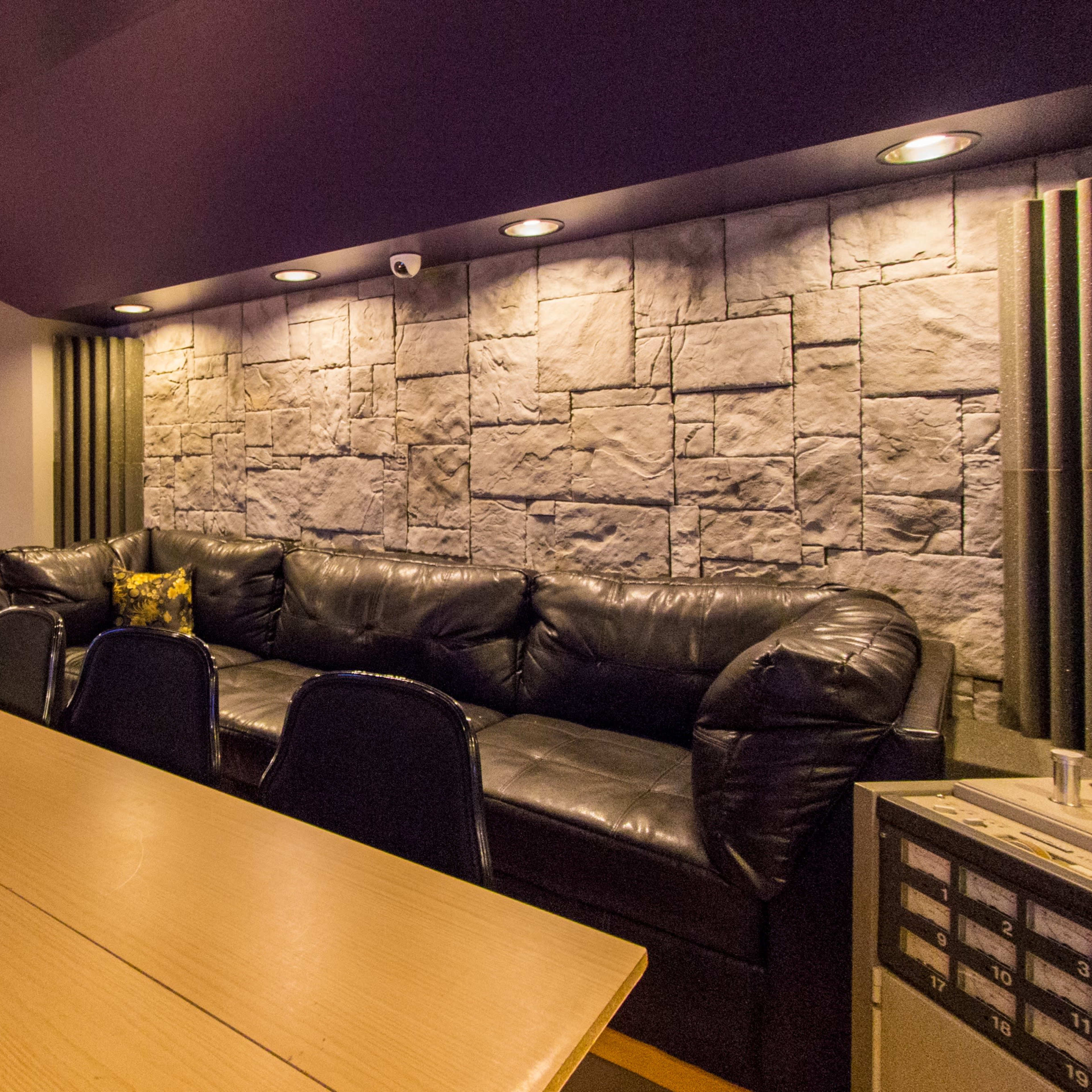 A dimly lit lounge area featuring a black leather sofa, a wooden bar counter, and a stone wall with recessed lighting.