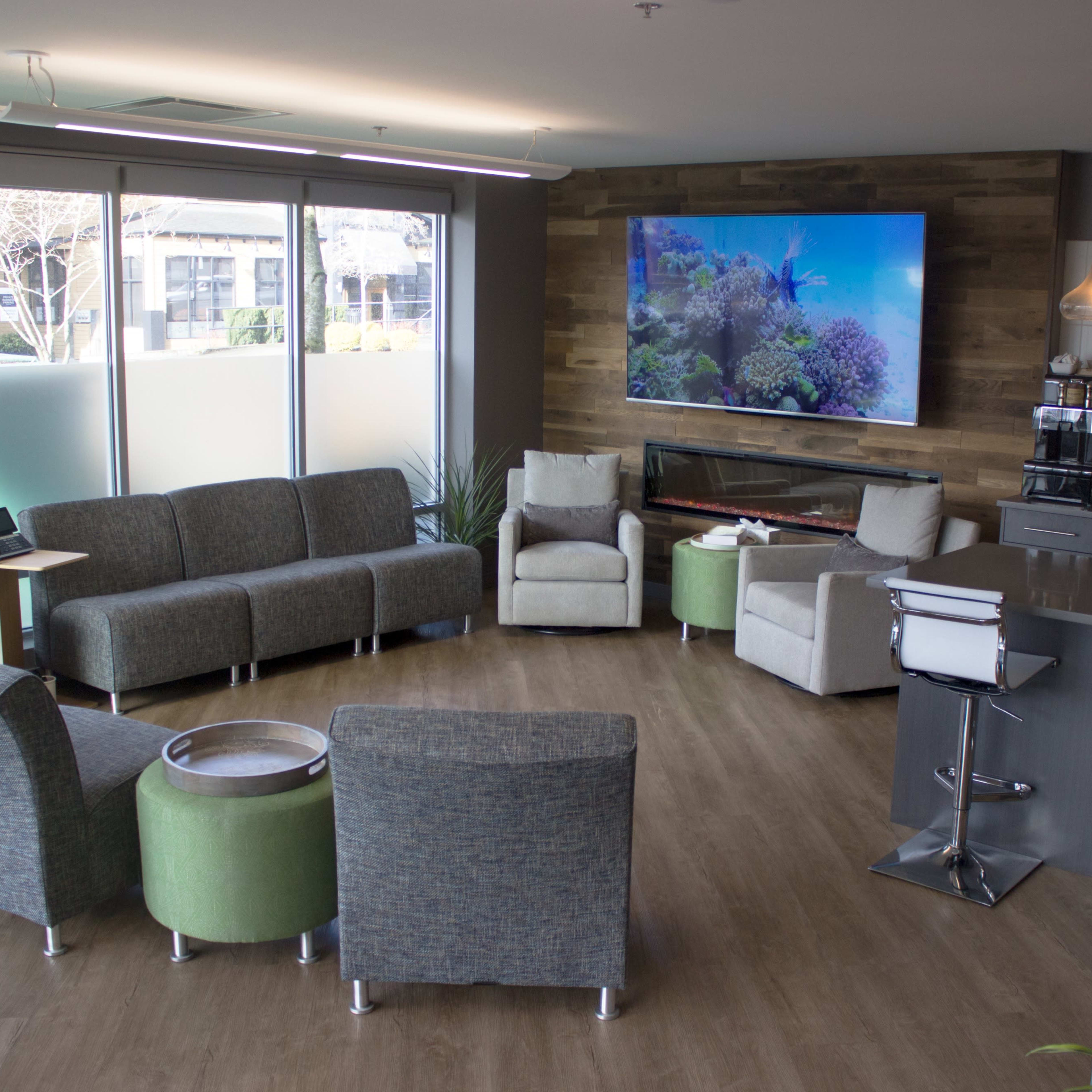A modern, informal lounge area with a variety of seating options, a television displaying an underwater scene, and a kitchenette in the background.