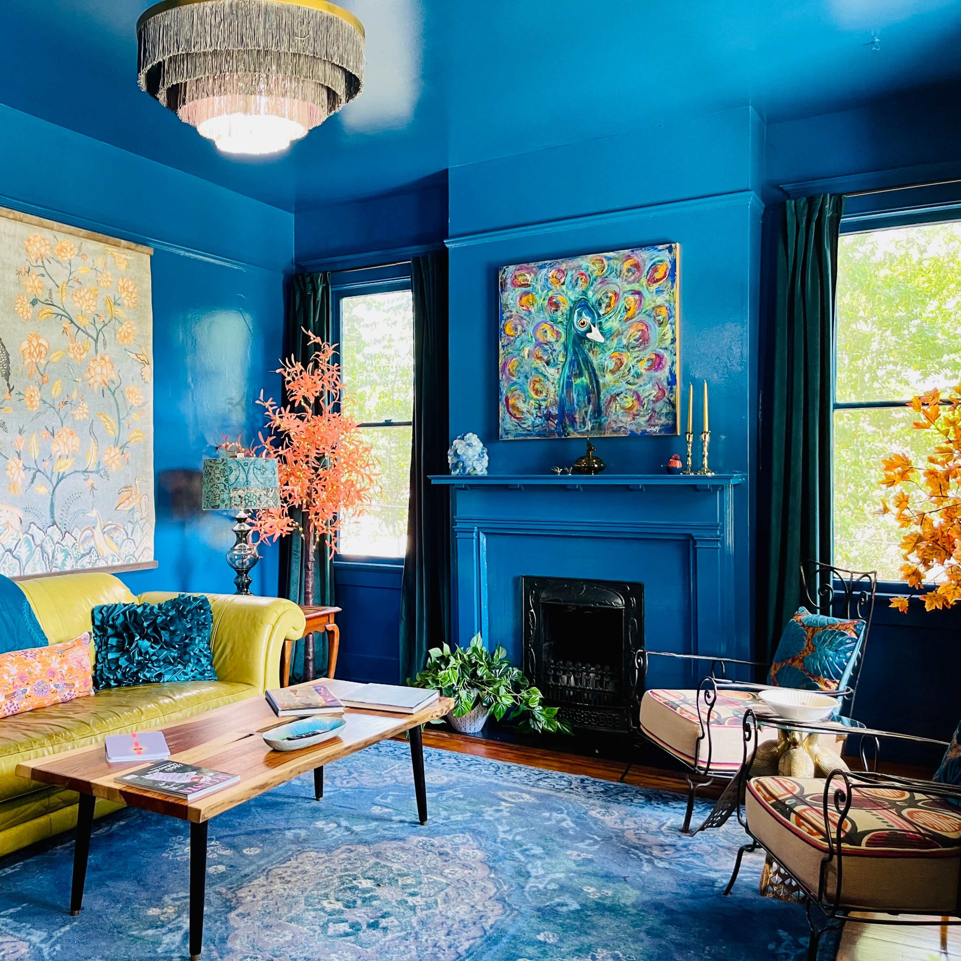 The room features a vibrant blue wall, a yellow couch, and decorative artwork complemented by plants and a fireplace.