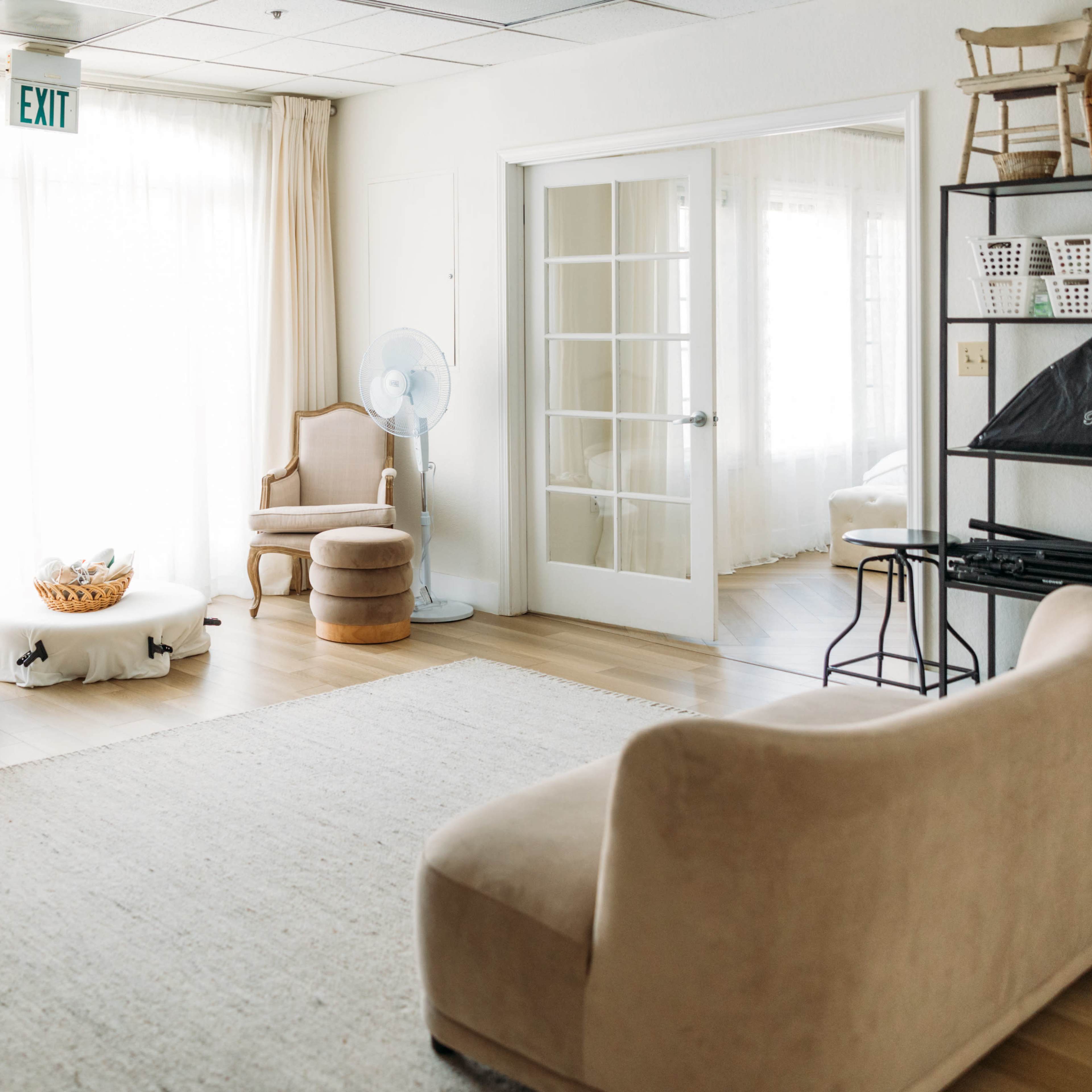 A bright room with large windows, featuring a light-colored rug, a sofa, a chair, and a small table.