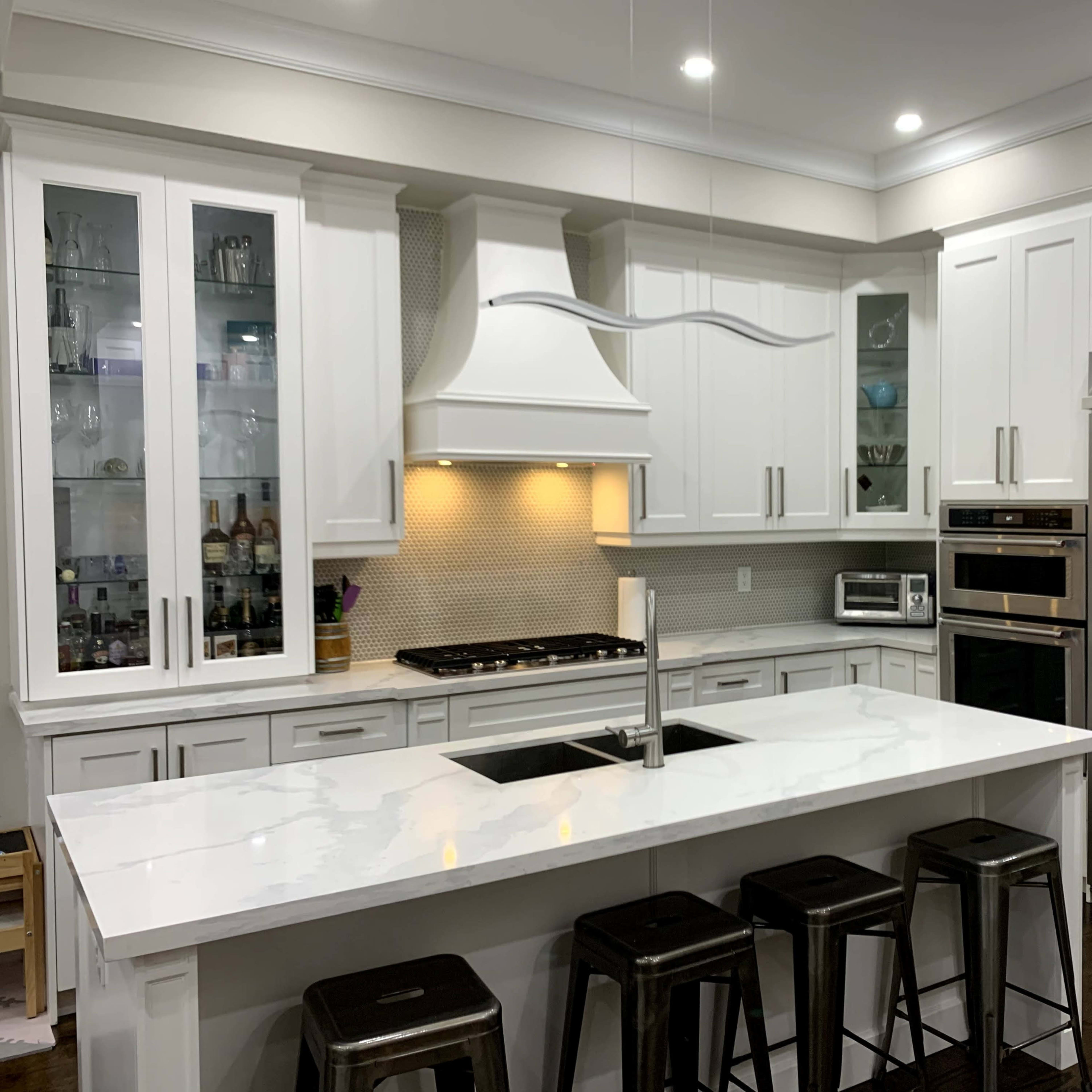 A modern kitchen with white cabinets, a large island with bar stools, stainless steel appliances, and a hood above the stove.