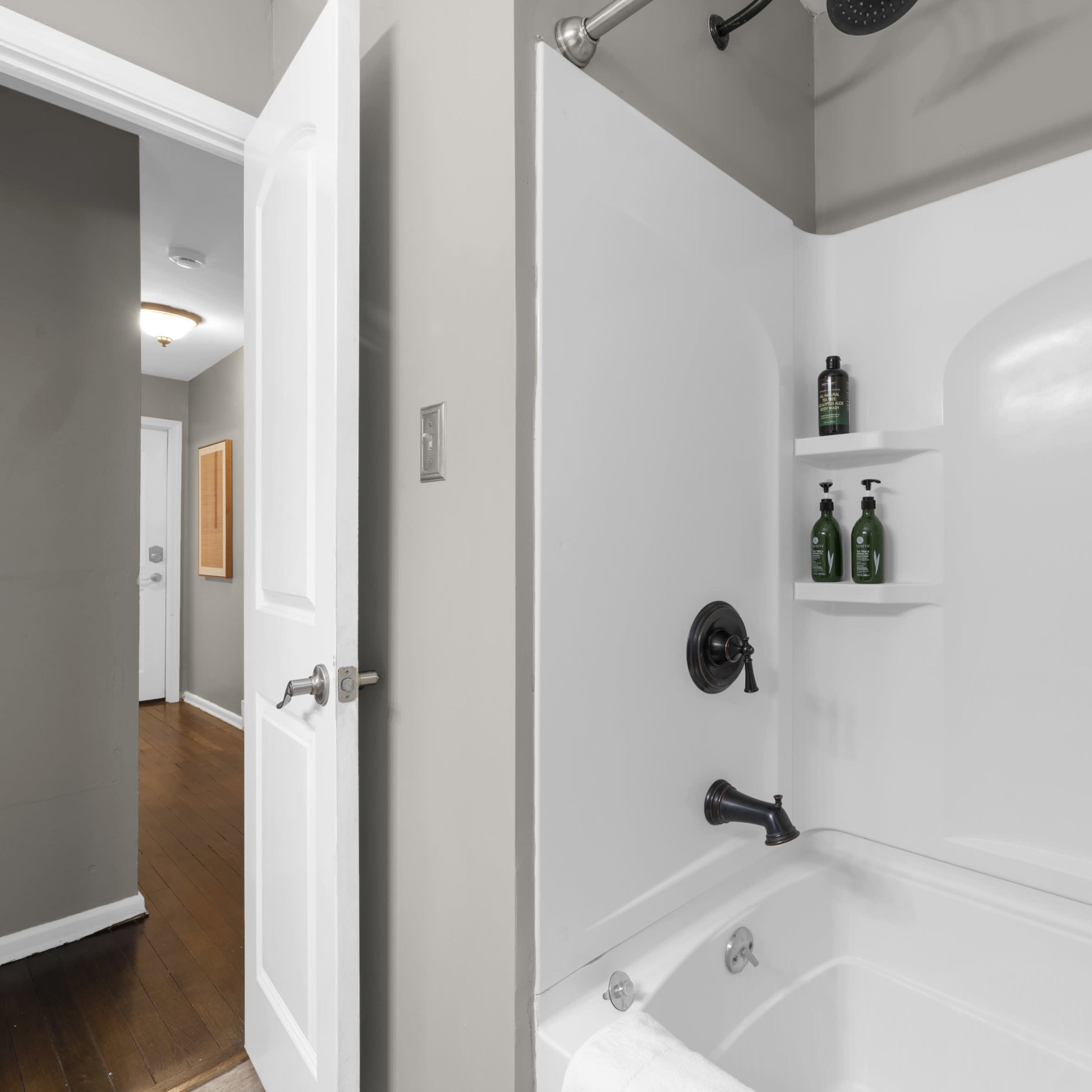 A clean bathroom featuring a white bathtub with a showerhead and shelves holding green bottles.