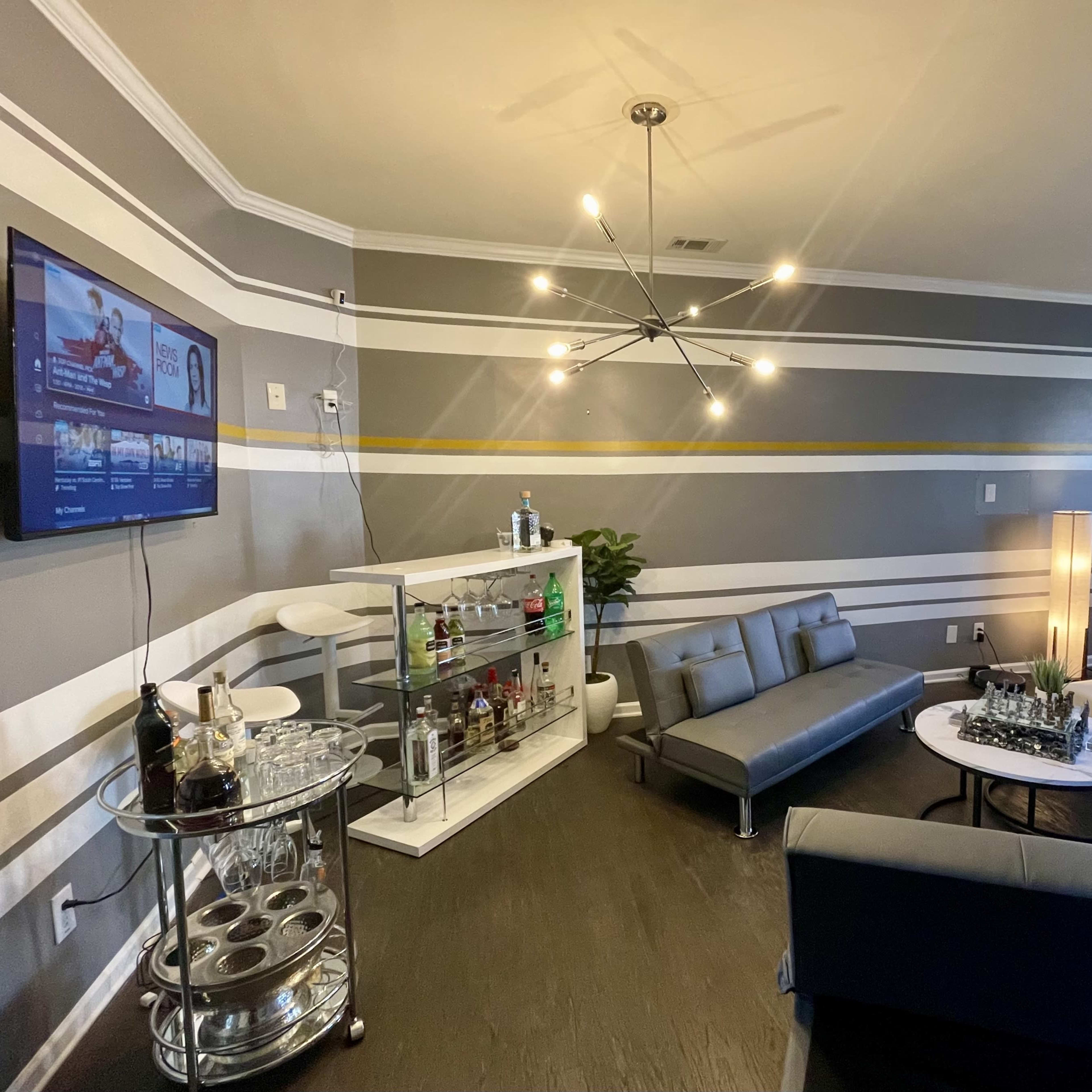 A modern living room with a sectional sofa, a white couch, and a glass cabinet displaying various bottles, all set against gray walls with yellow and white stripes.
