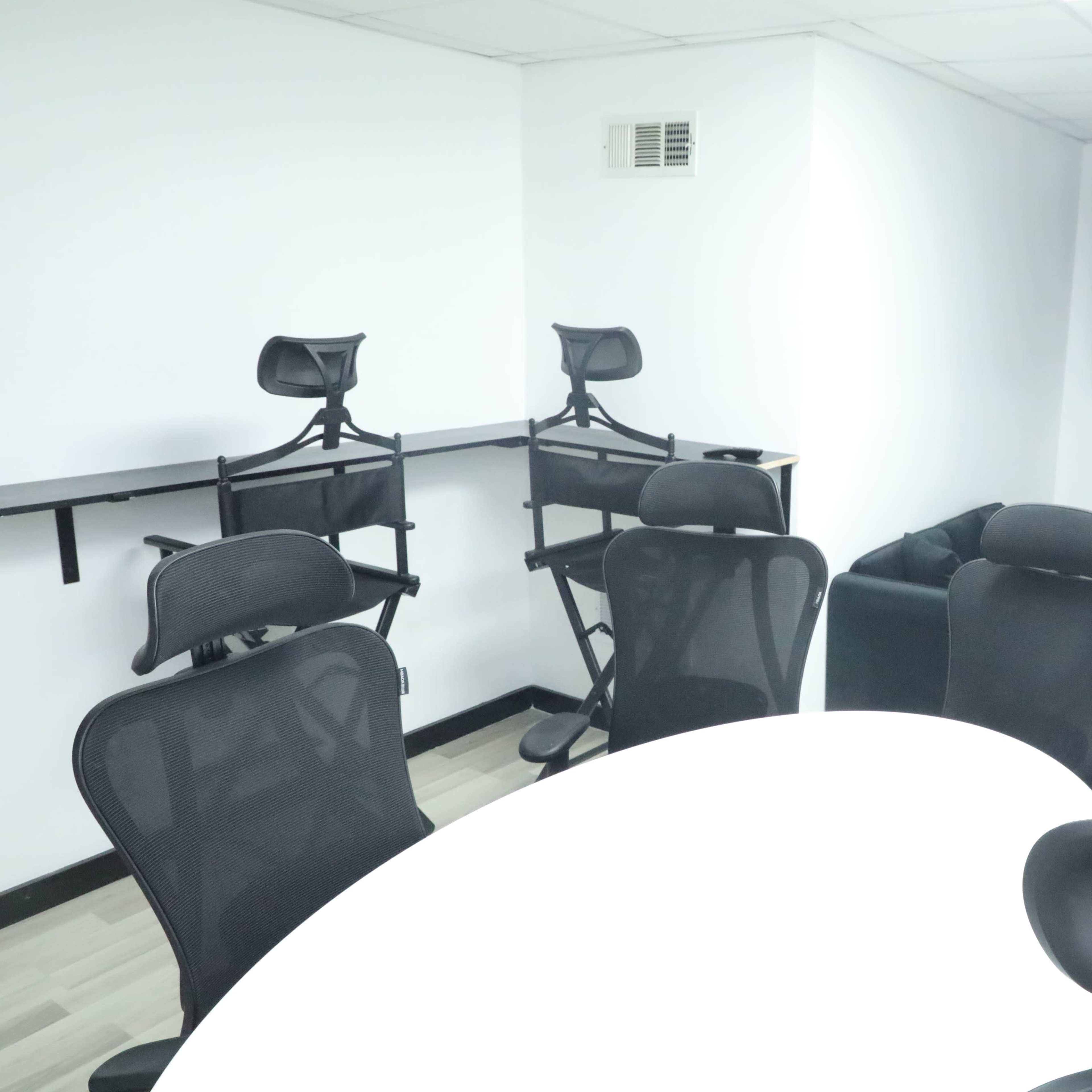 A modern meeting room with a white oval table, black chairs, and a wall-mounted flat-screen TV.