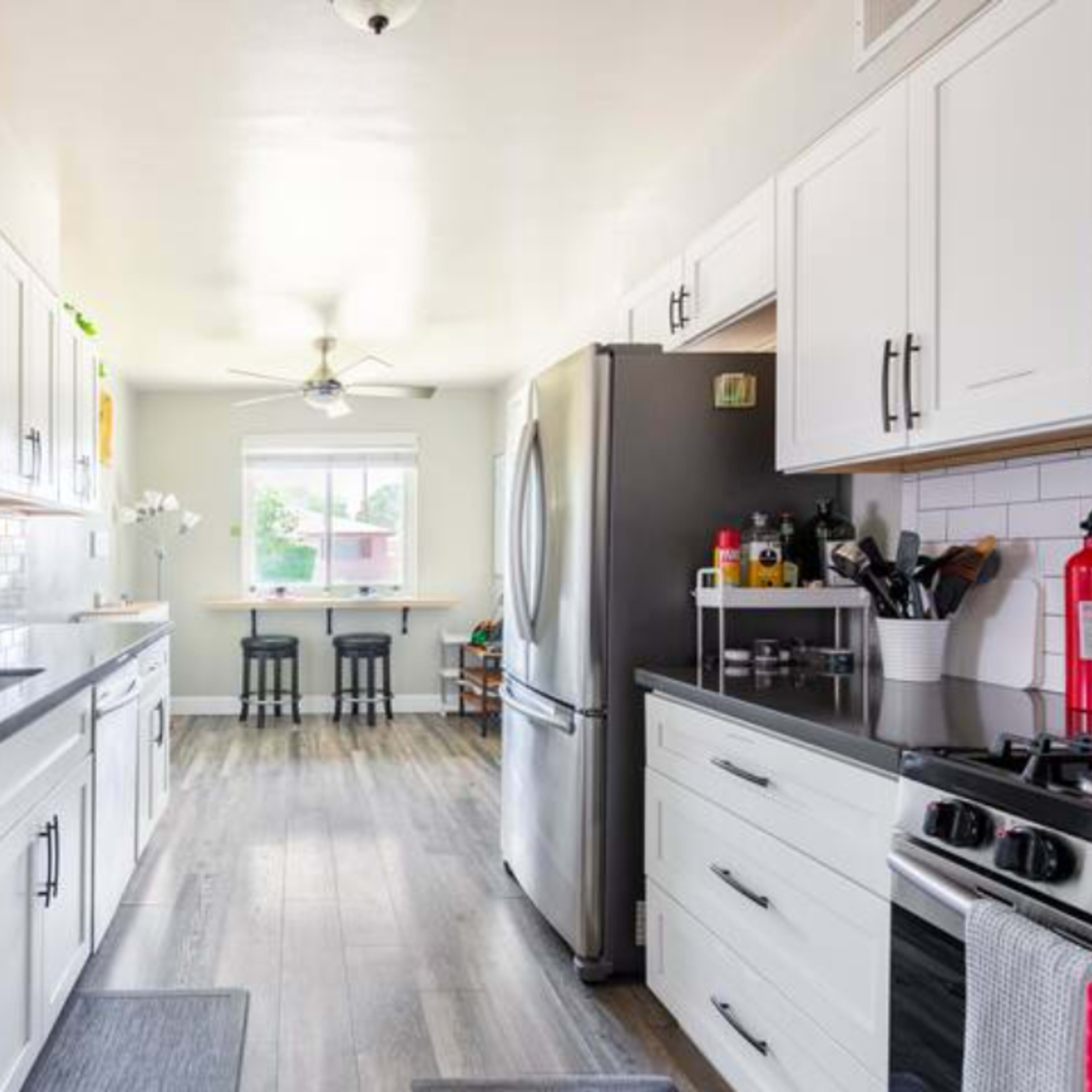 A modern kitchen featuring white cabinetry, stainless steel appliances, and a breakfast bar with two stools.