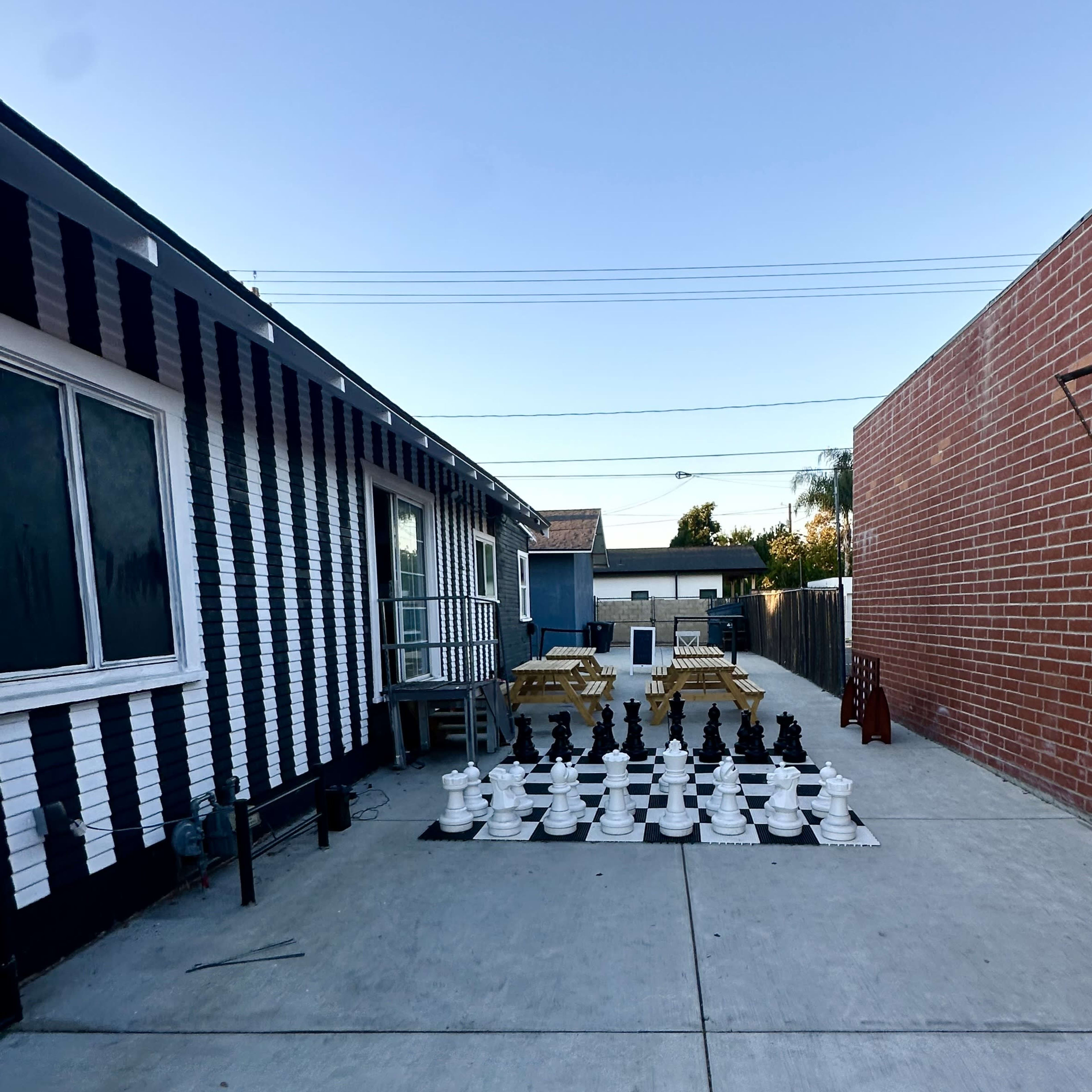 A large outdoor space features a striped building, a chessboard with oversized pieces, and seating areas in the background.