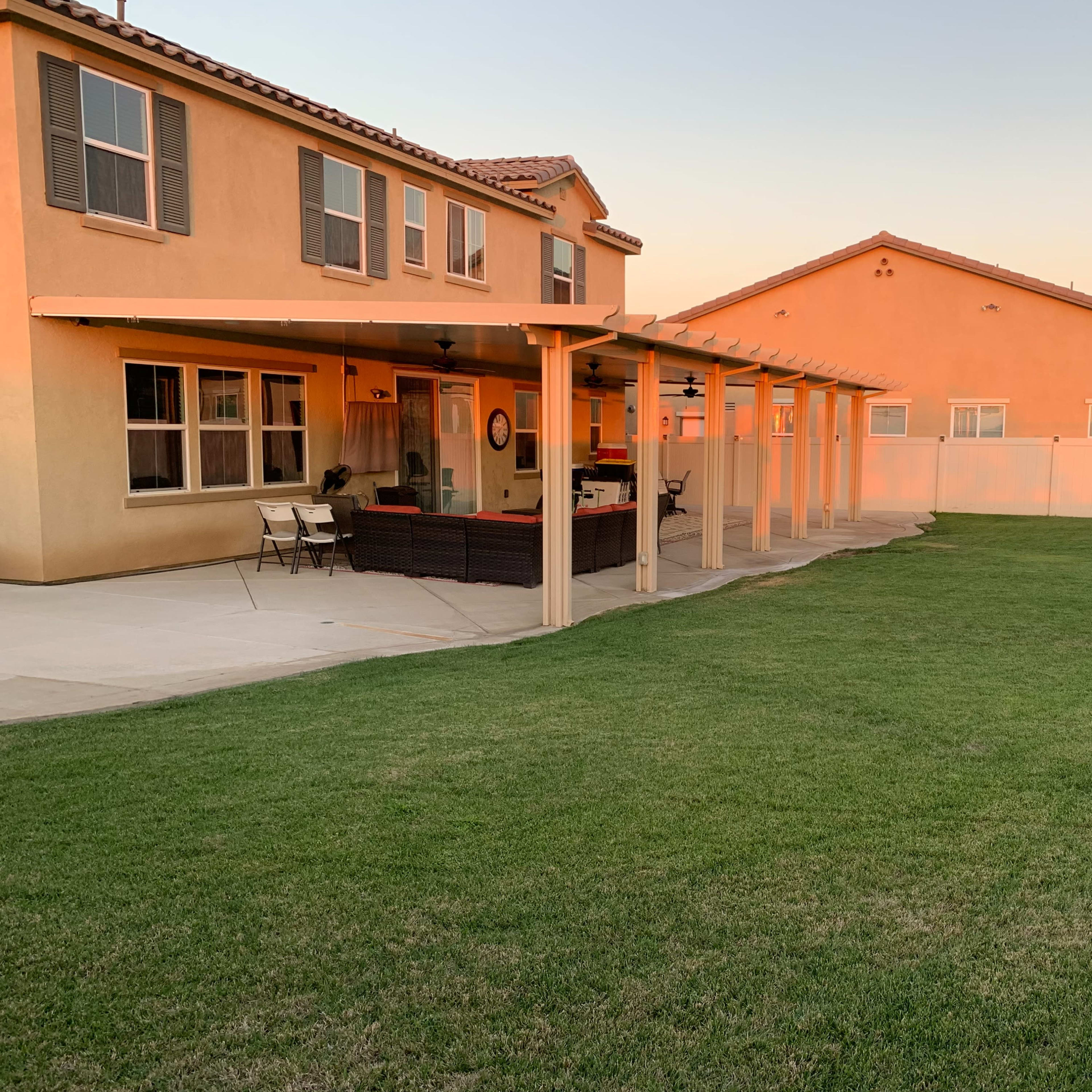 A backyard with a patio covered by a pergola, adjacent to two houses and a grassy lawn.