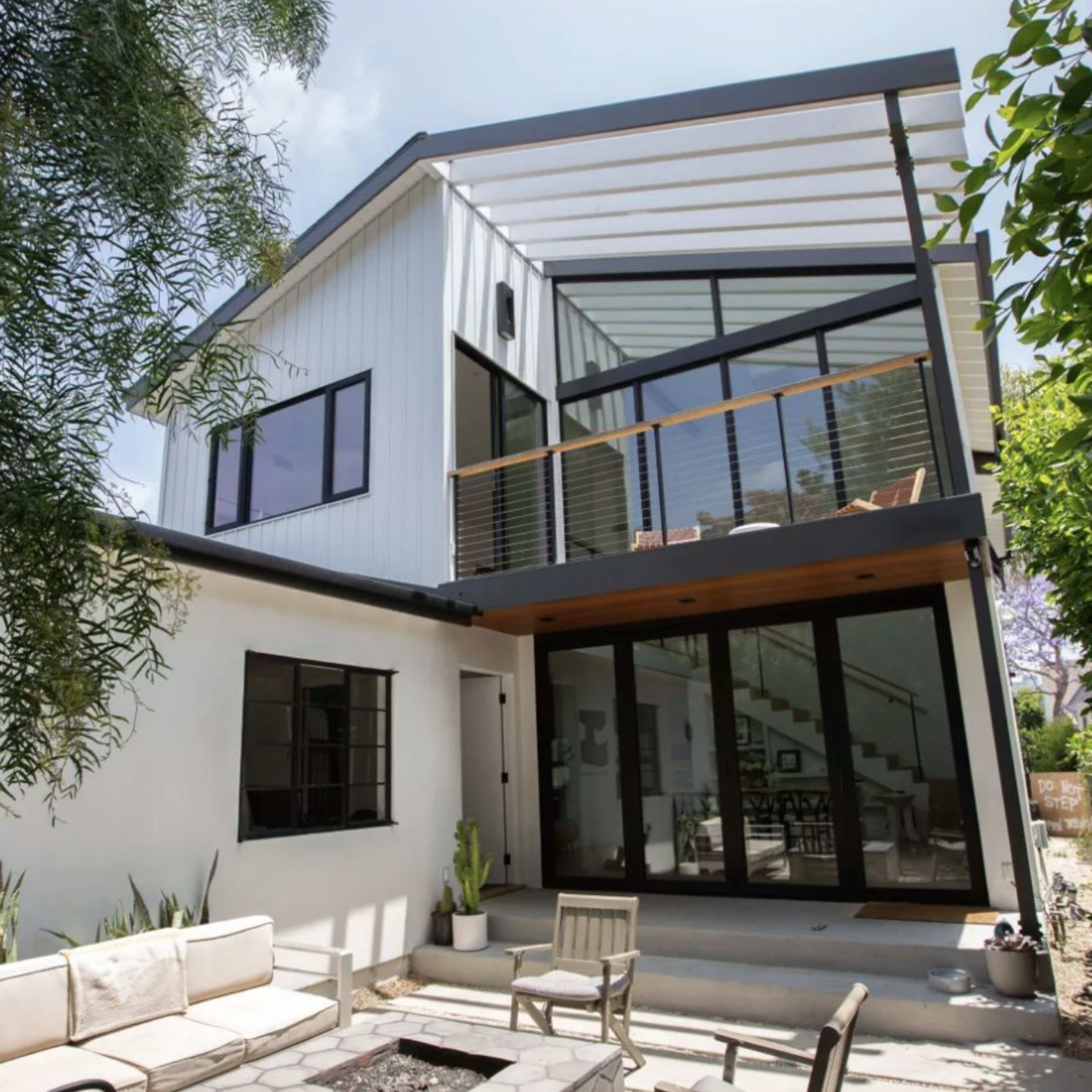 A modern two-story house with a combination of white and dark exterior elements, featuring large windows and a balcony.
