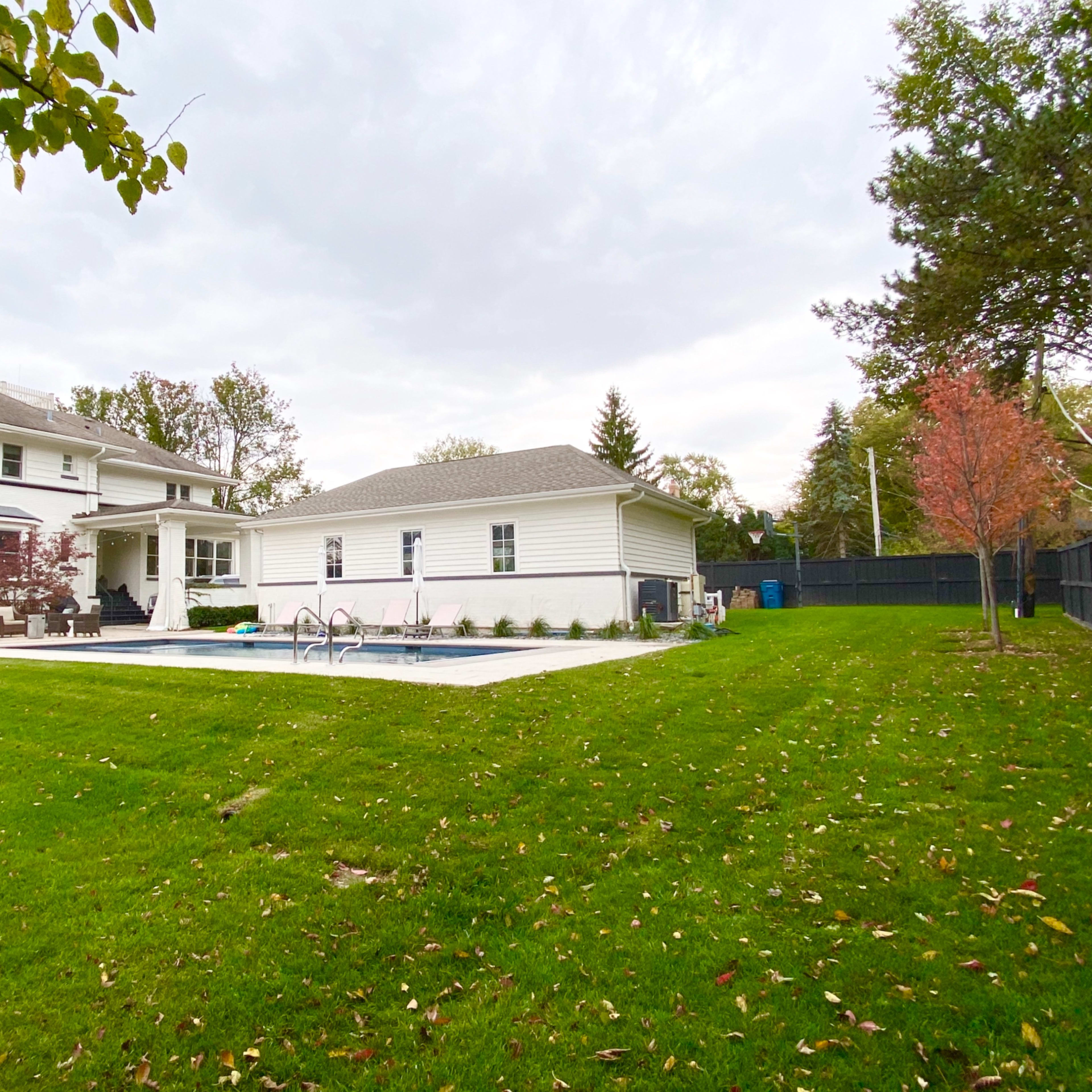 A spacious backyard features a swimming pool beside a single-story house and a two-story home in the background.