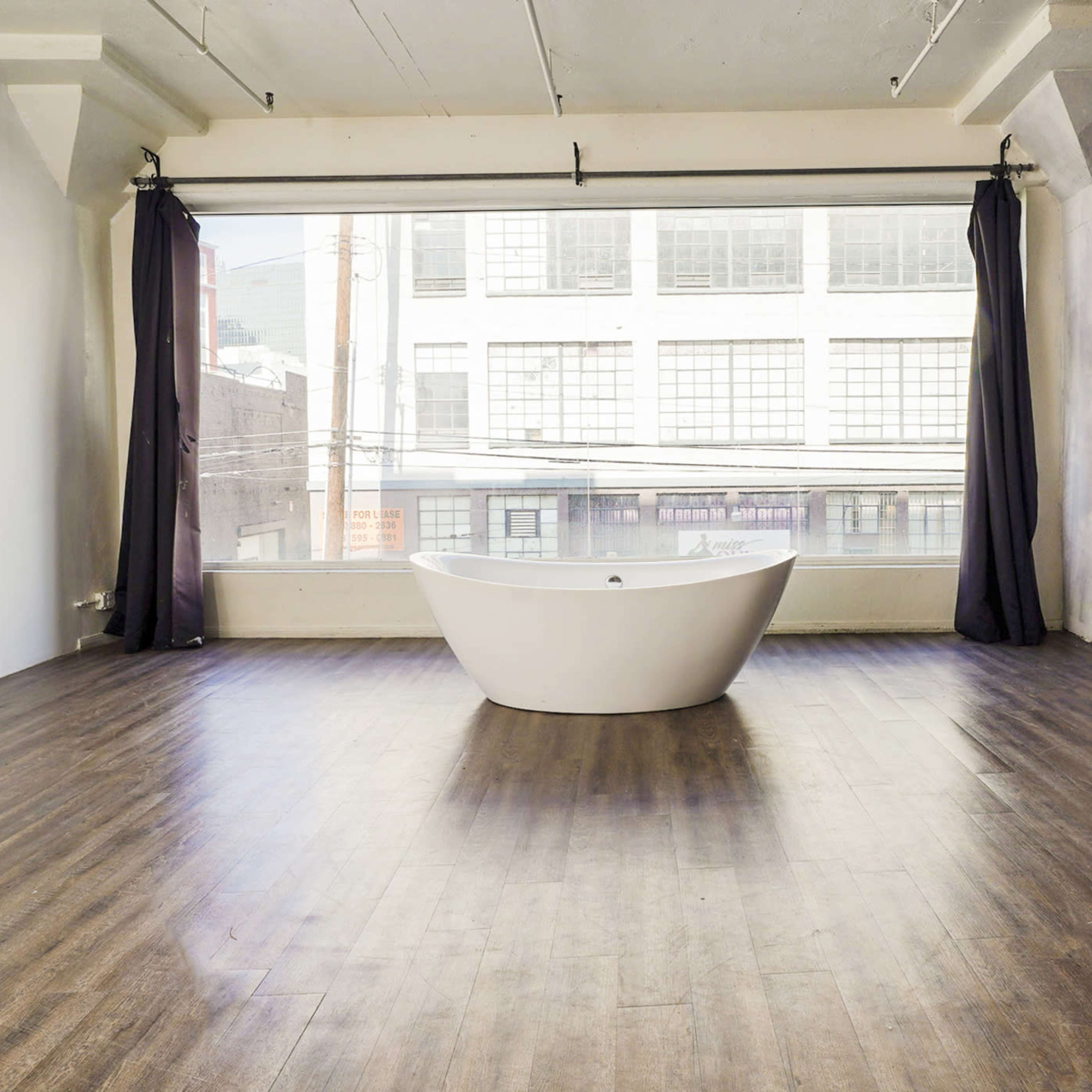 A spacious room with a freestanding white bathtub, large windows, and wooden flooring.