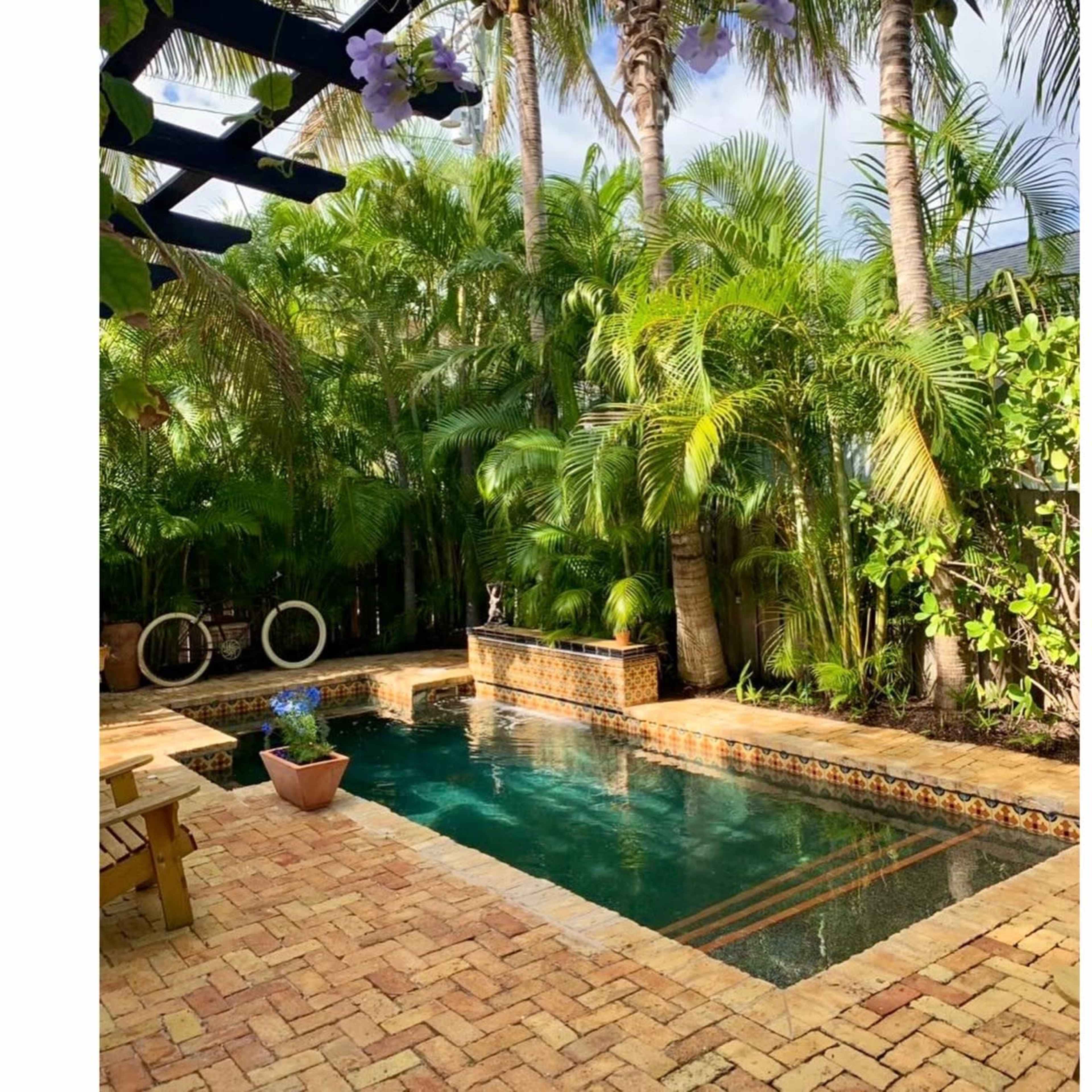 A small, rectangular swimming pool surrounded by lush tropical plants and a brick patio.