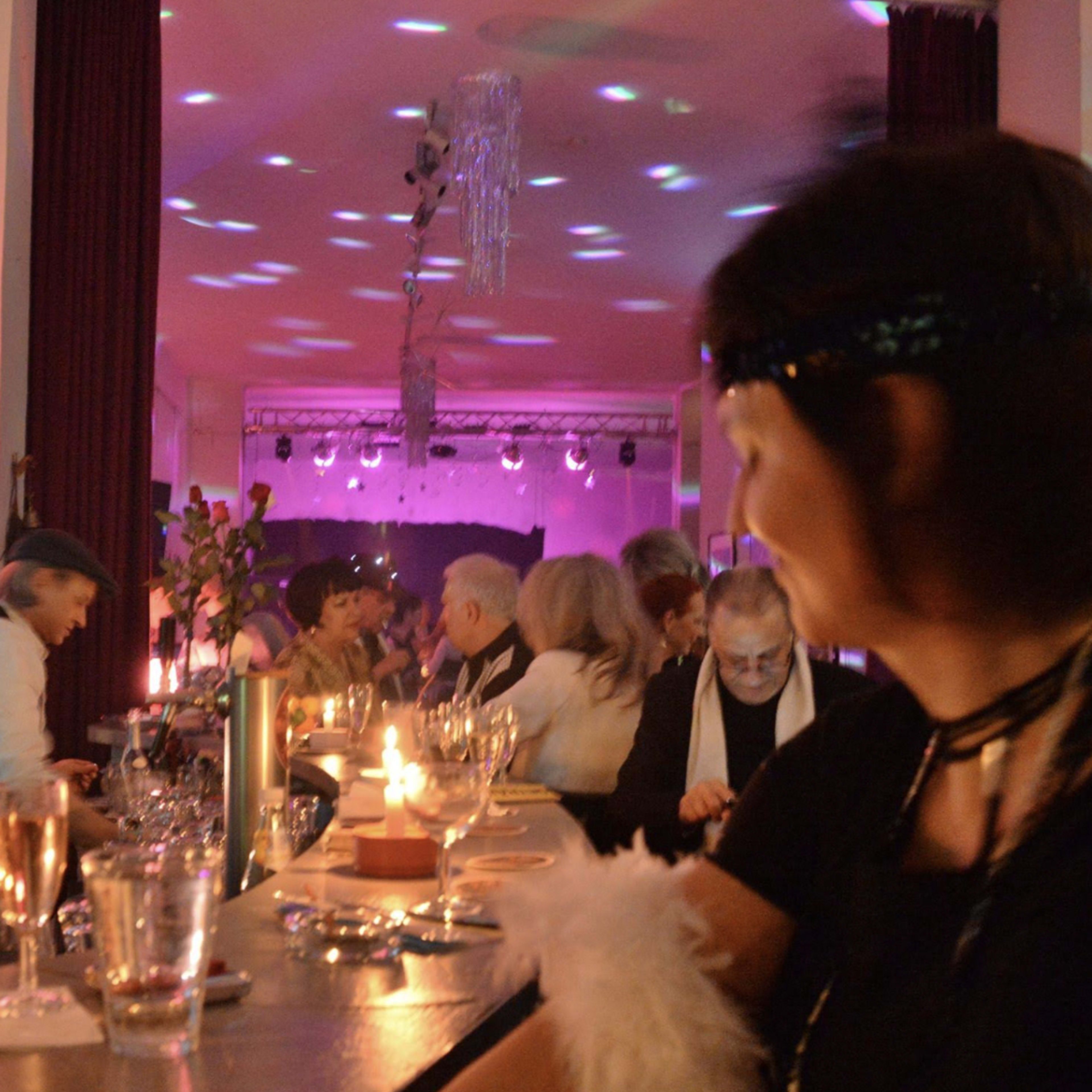A lively gathering is depicted at a bar, with guests enjoying drinks and colorful lights illuminating the scene.