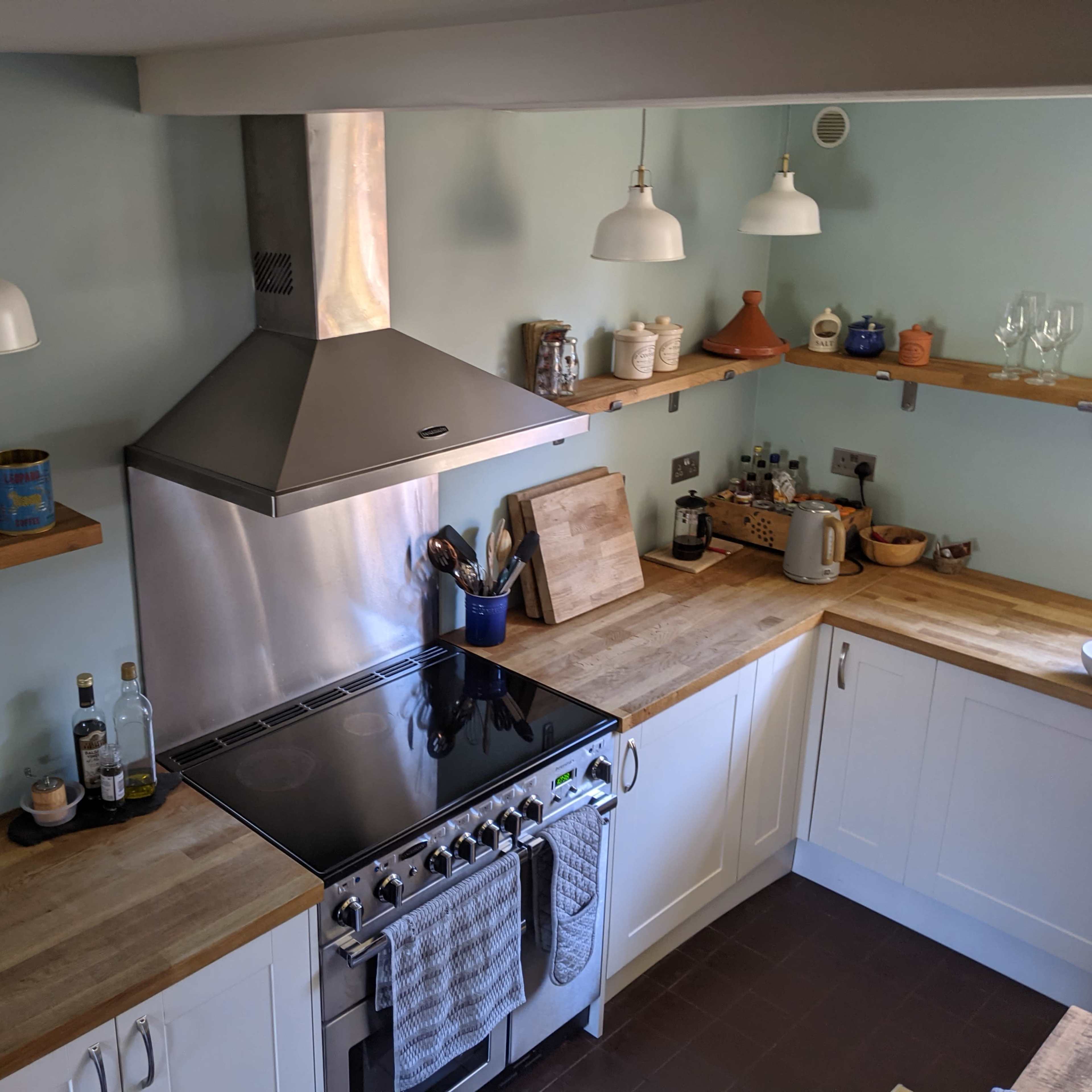 A modern kitchen with a stainless steel hood over a gas stove, wooden countertops, and light green walls.