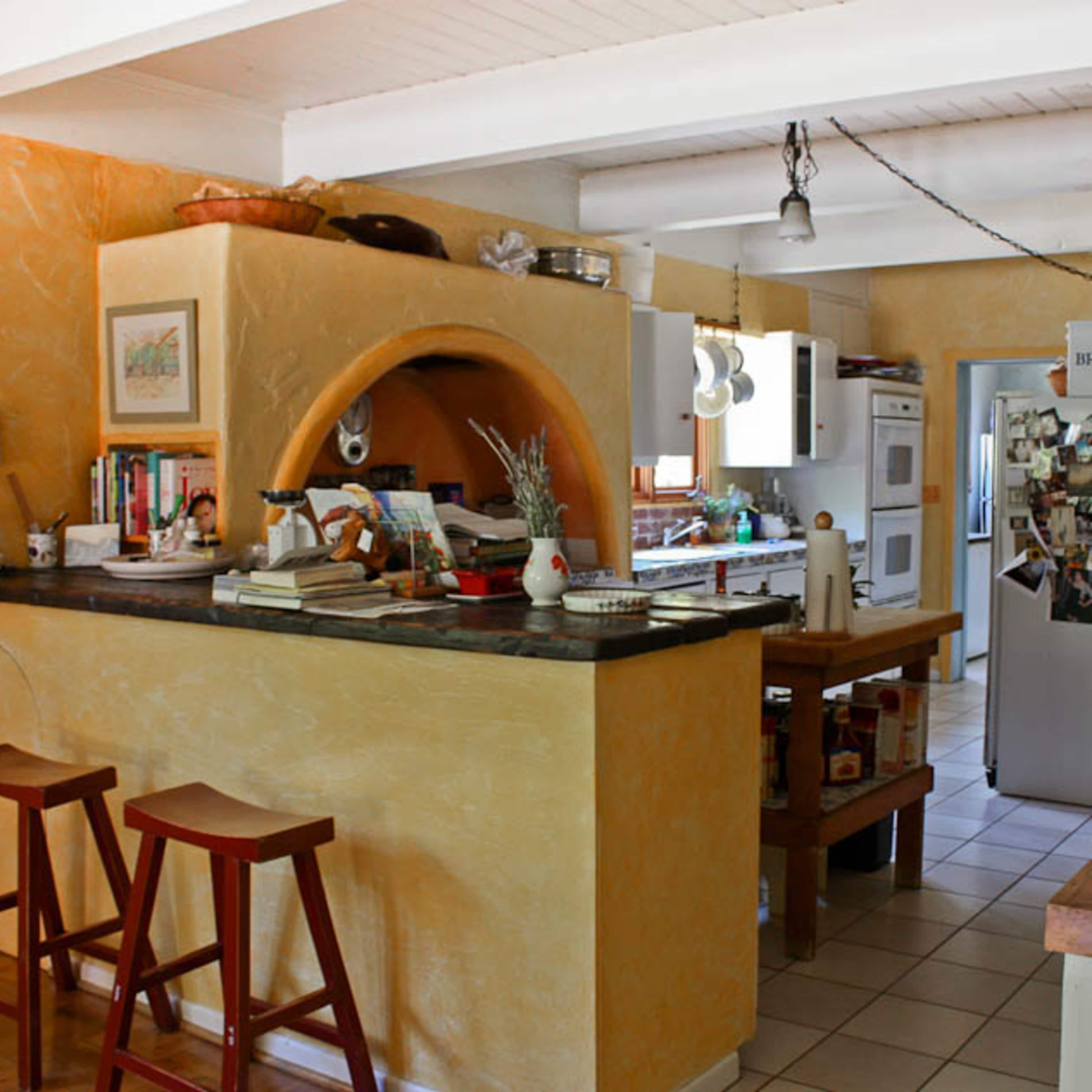 A modern kitchen with a breakfast bar, wooden stools, and an open layout featuring various appliances and shelves.