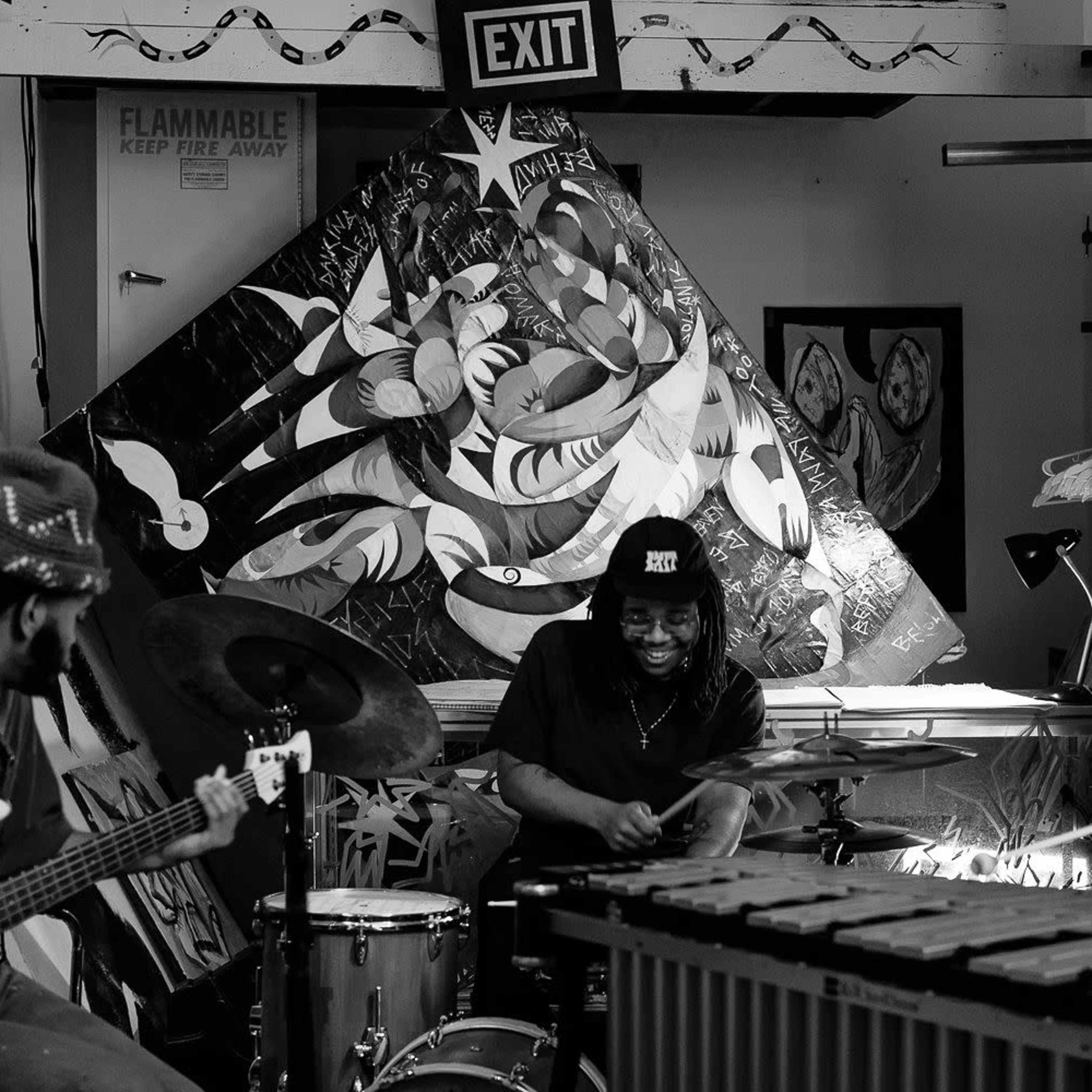 A band performs in an art studio surrounded by large, colorful paintings.
