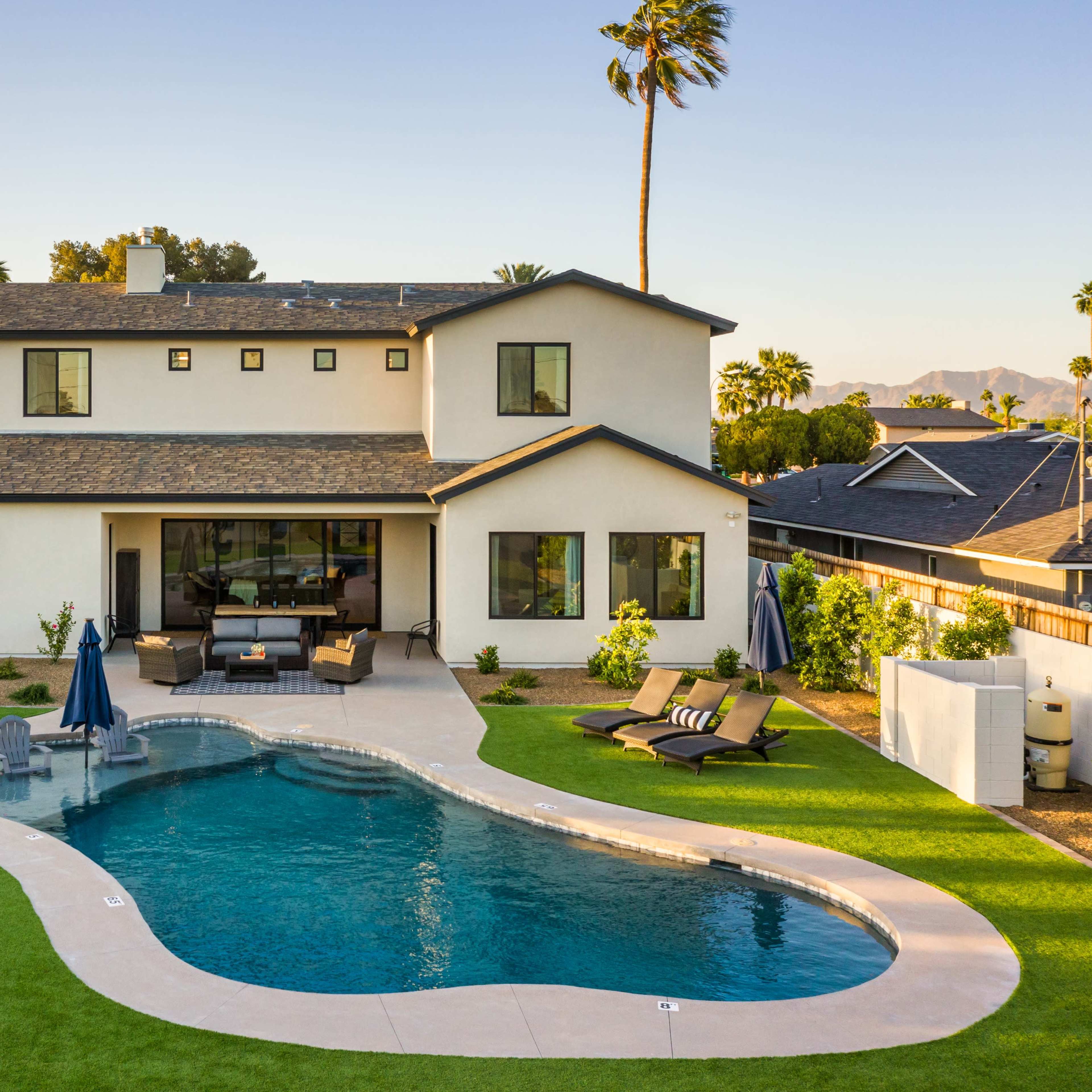 A modern two-story house features a landscaped backyard with a curved swimming pool and patio area.