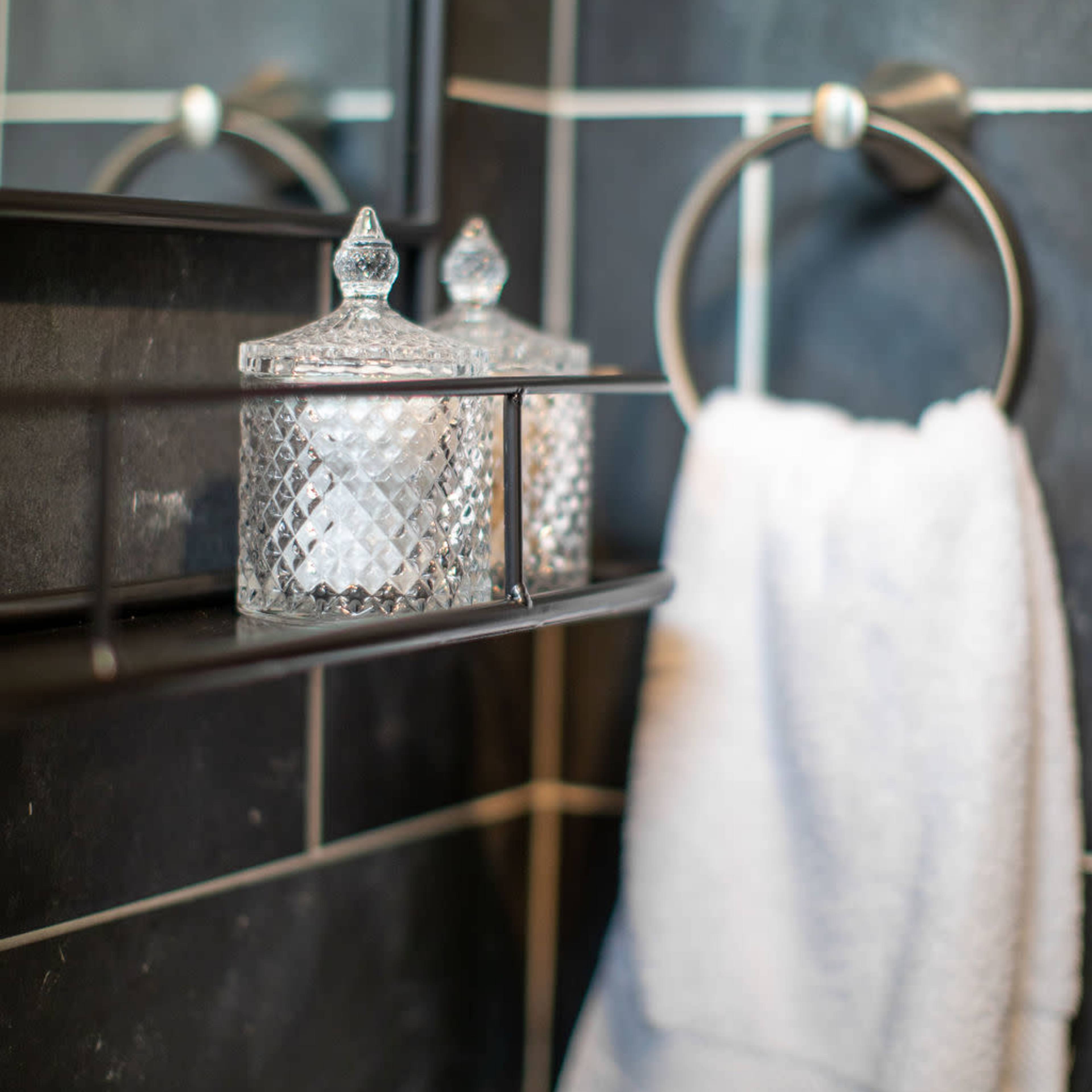 A bathroom shelf with two crystal containers and a white towel hanging on a ring.