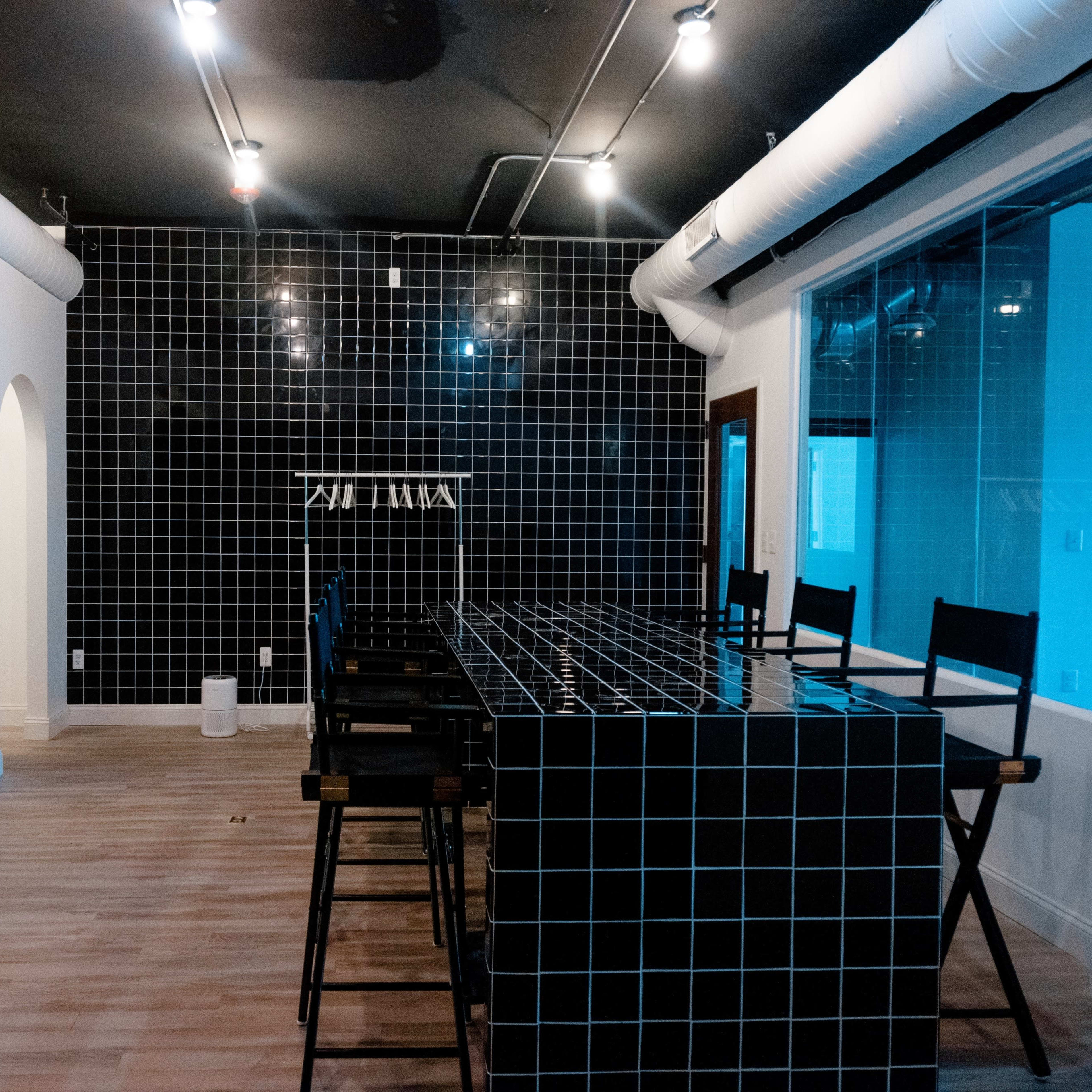 An empty room with a black tiled wall, a long black tiled bar, and several high stools arranged in front of it.