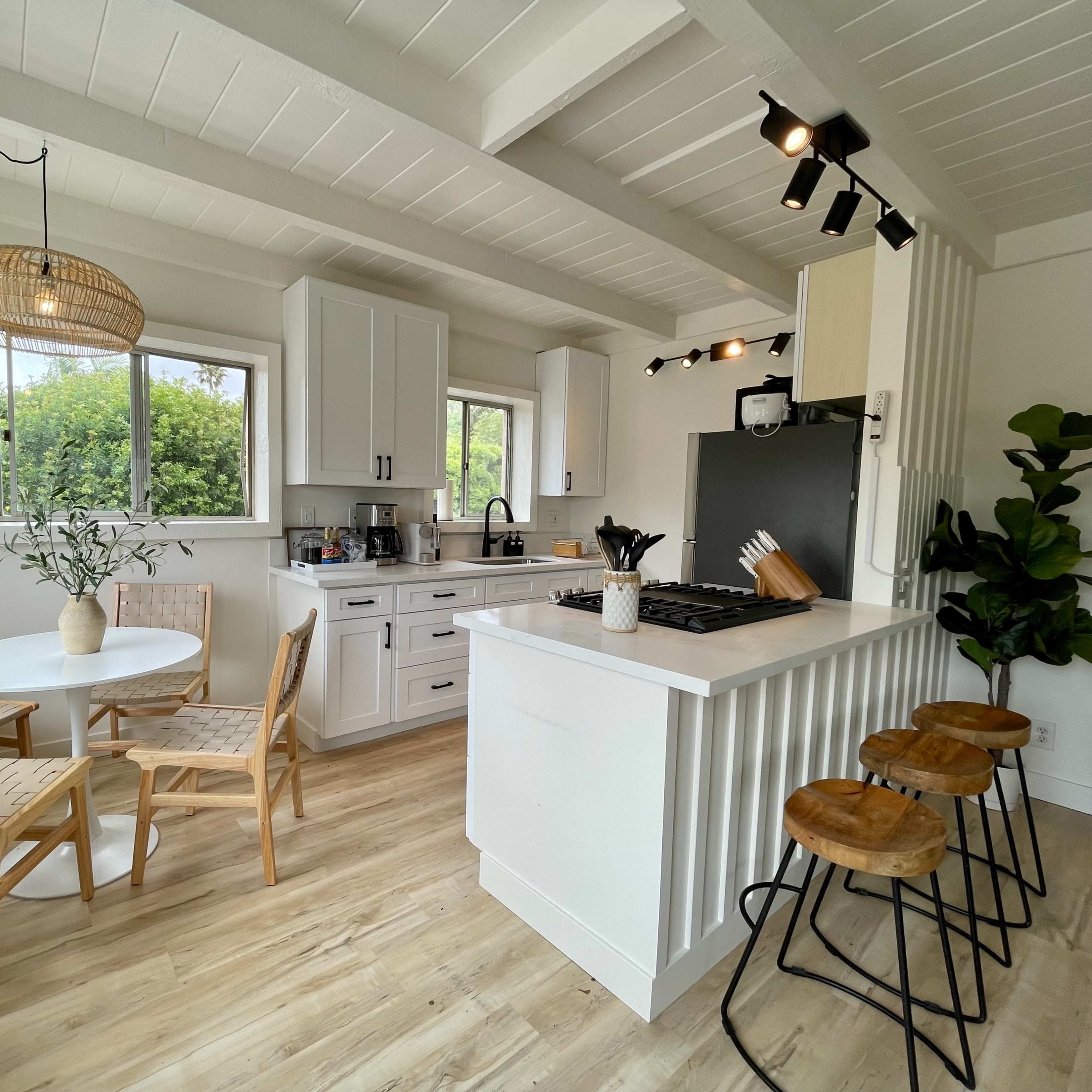 A bright kitchen features white cabinets, a gas stove, a small round dining table with wooden chairs, and bar stools at a counter.