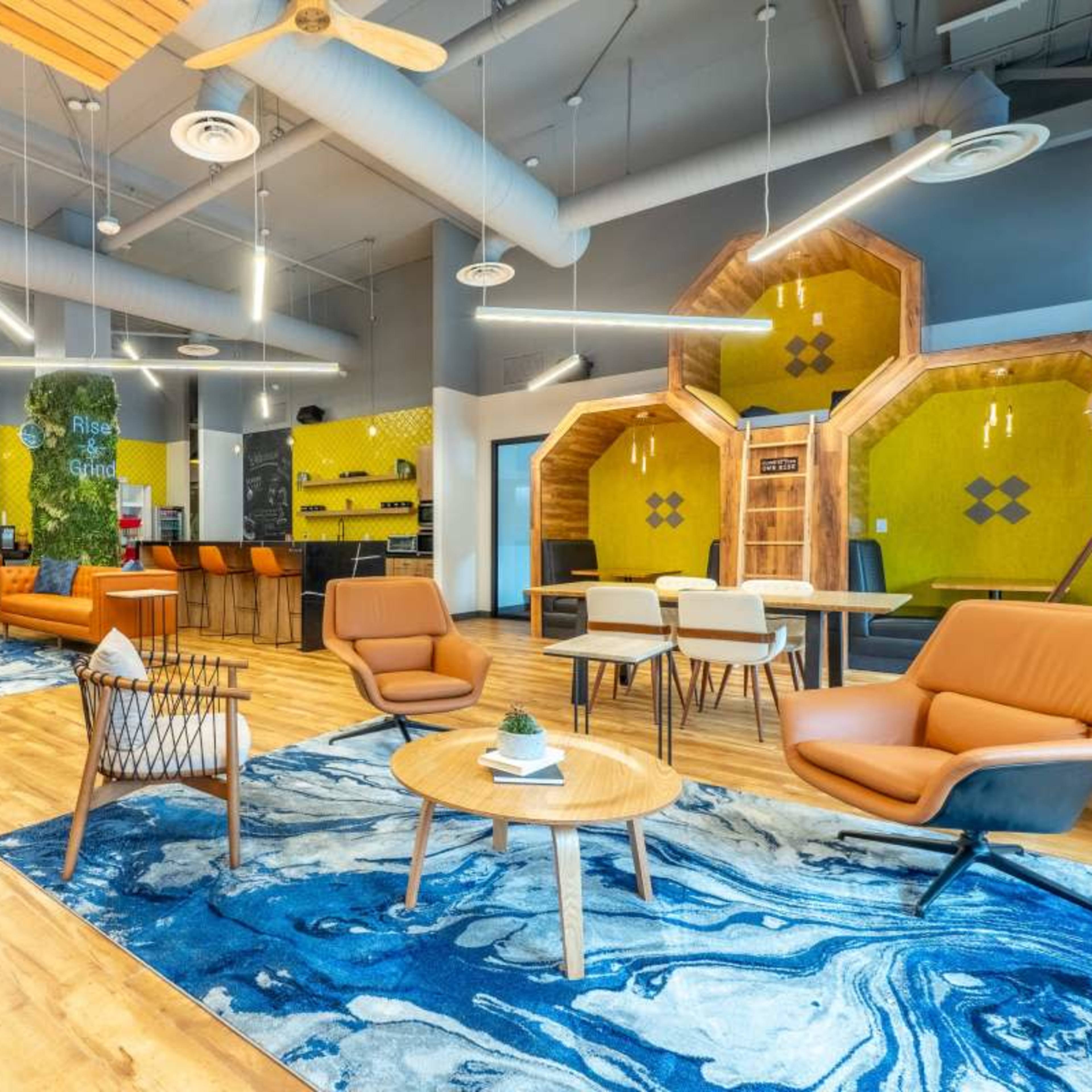 A modern co-working space featuring orange seating, wooden flooring, and a colorful hexagonal wall design.