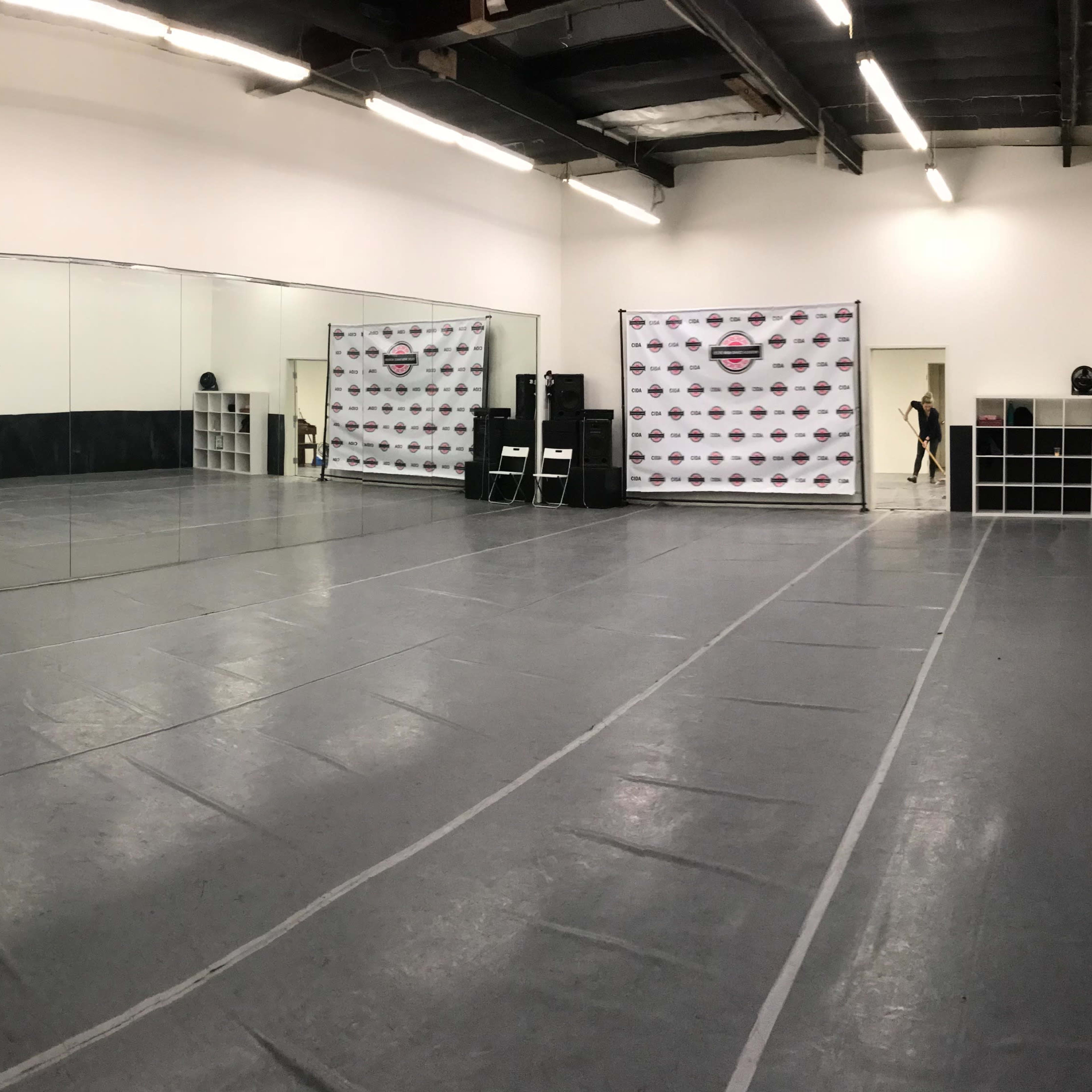A spacious dance studio with mirrors on one wall and a promotional backdrop against another wall.