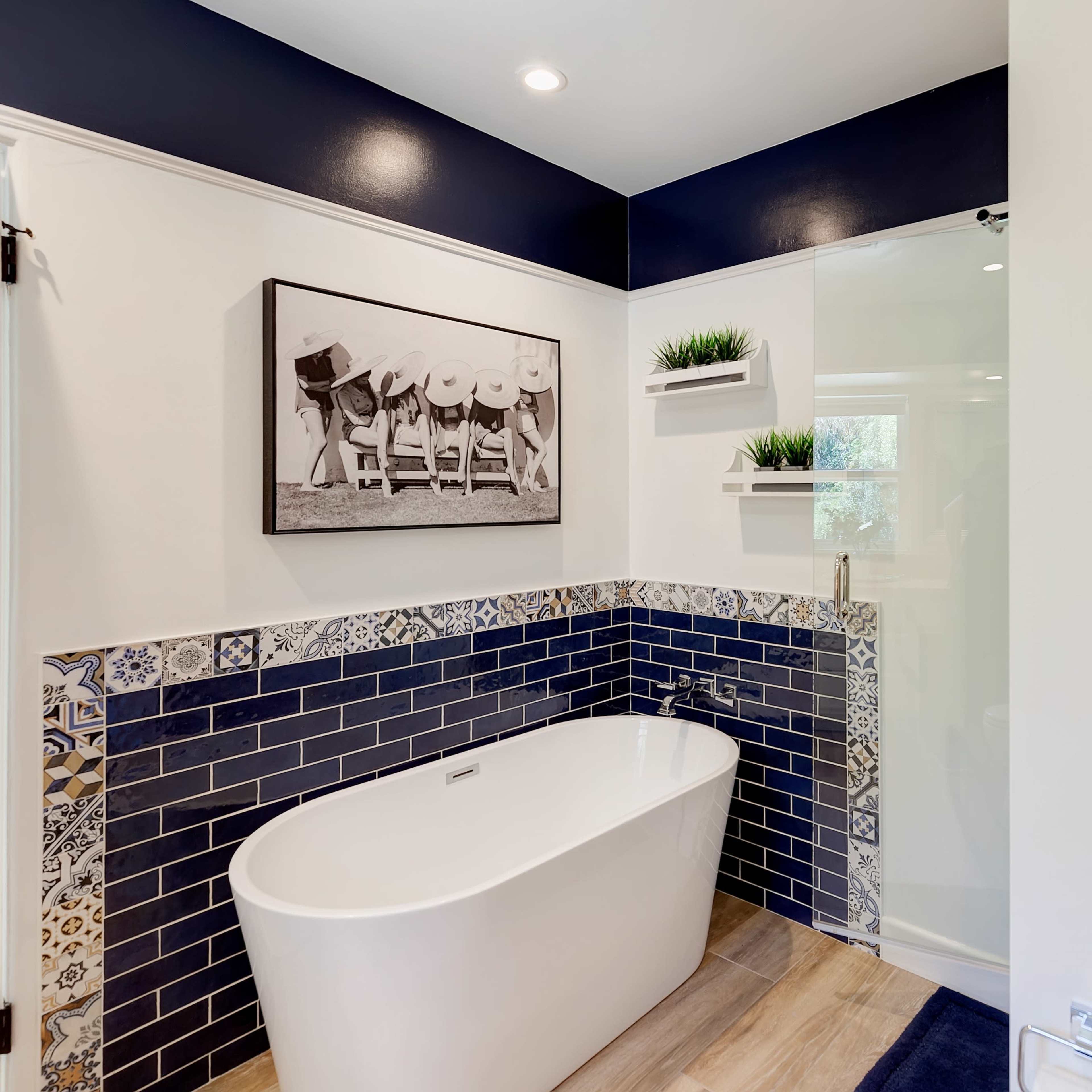 A modern bathroom with a freestanding white bathtub, dark navy walls, and decorative tile accents around the floor and base.