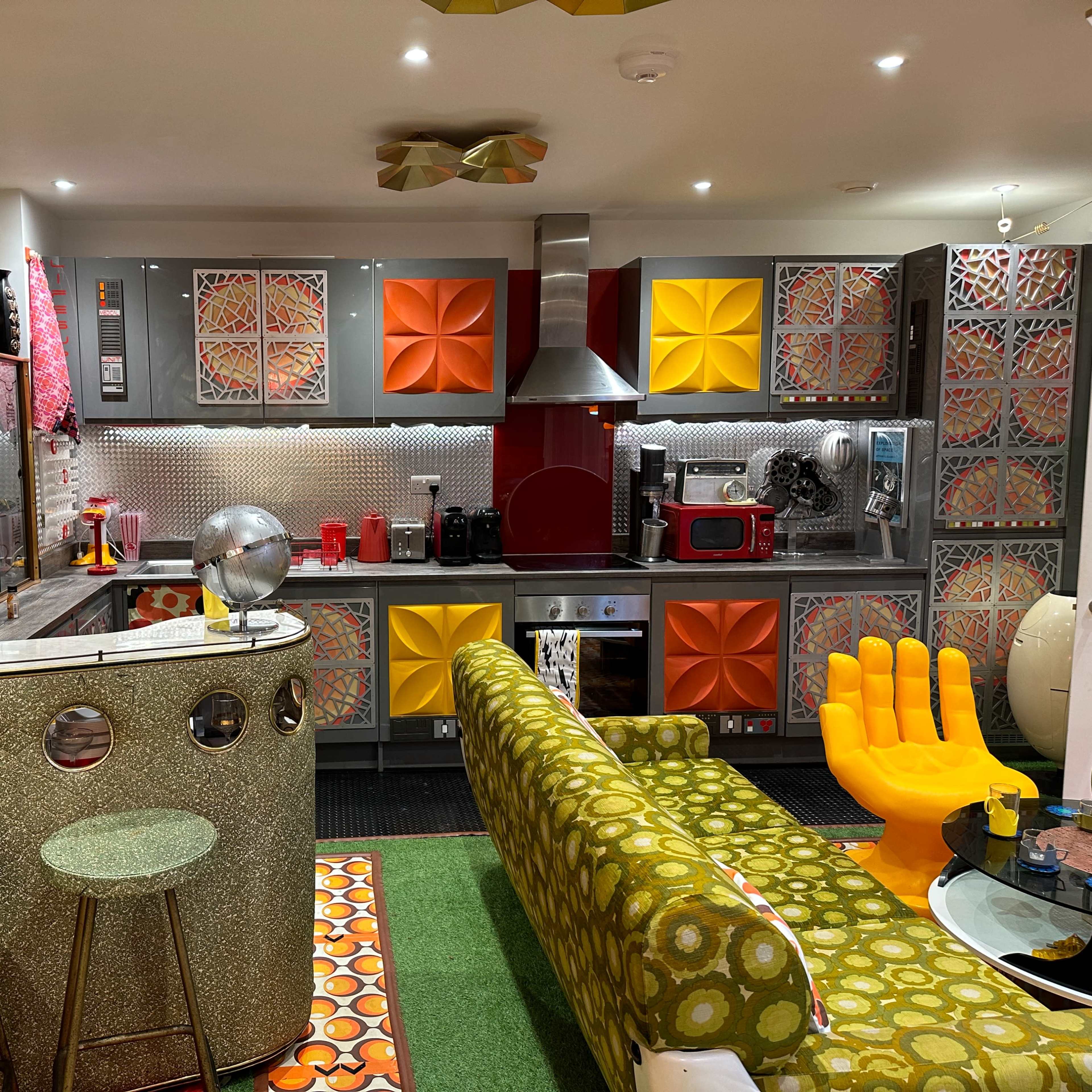 A colorful retro kitchen with patterned cabinetry, a circular bar, and a green sofa shaped like a hand.