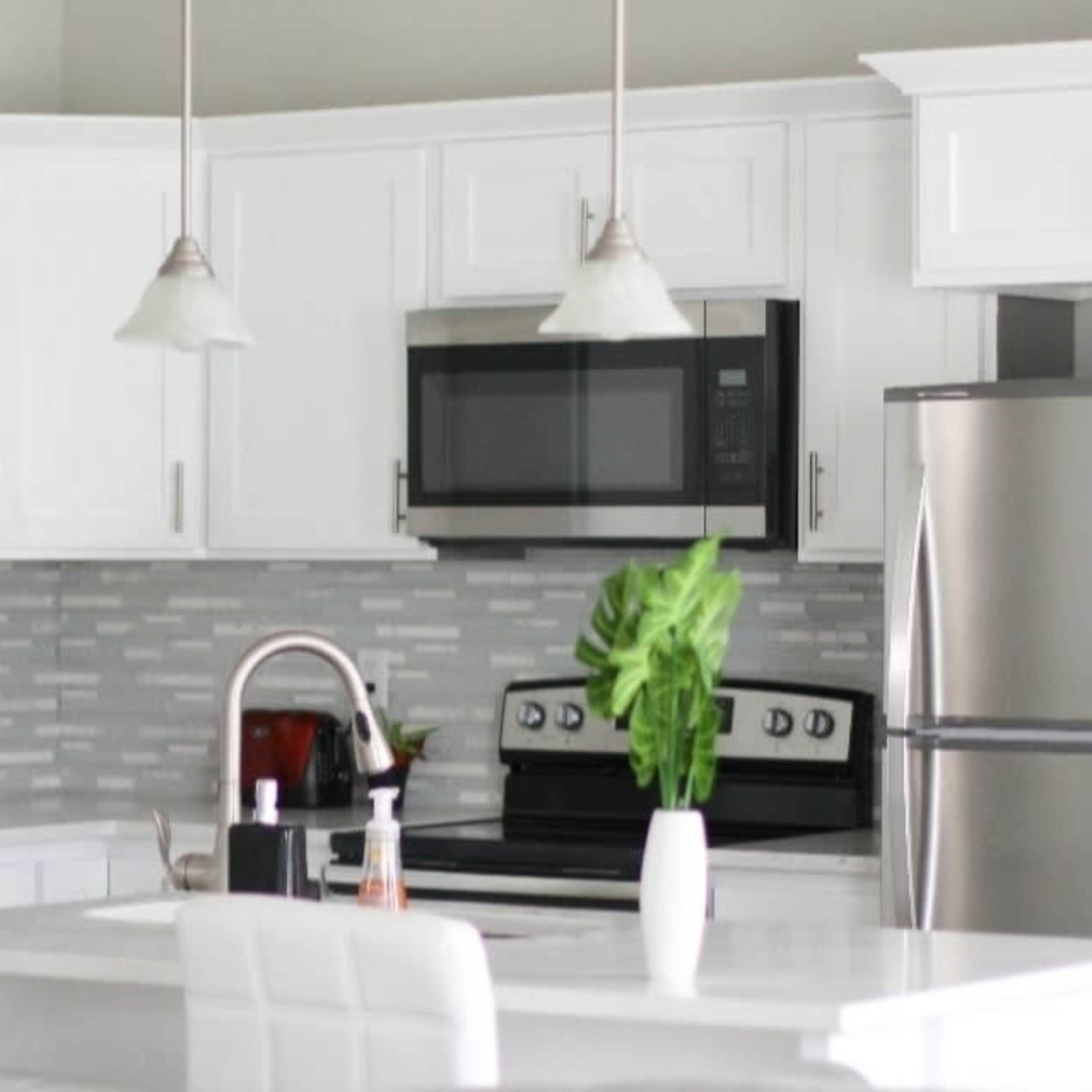 A modern kitchen with white cabinetry, stainless steel appliances, and a countertop island with bar stools.
