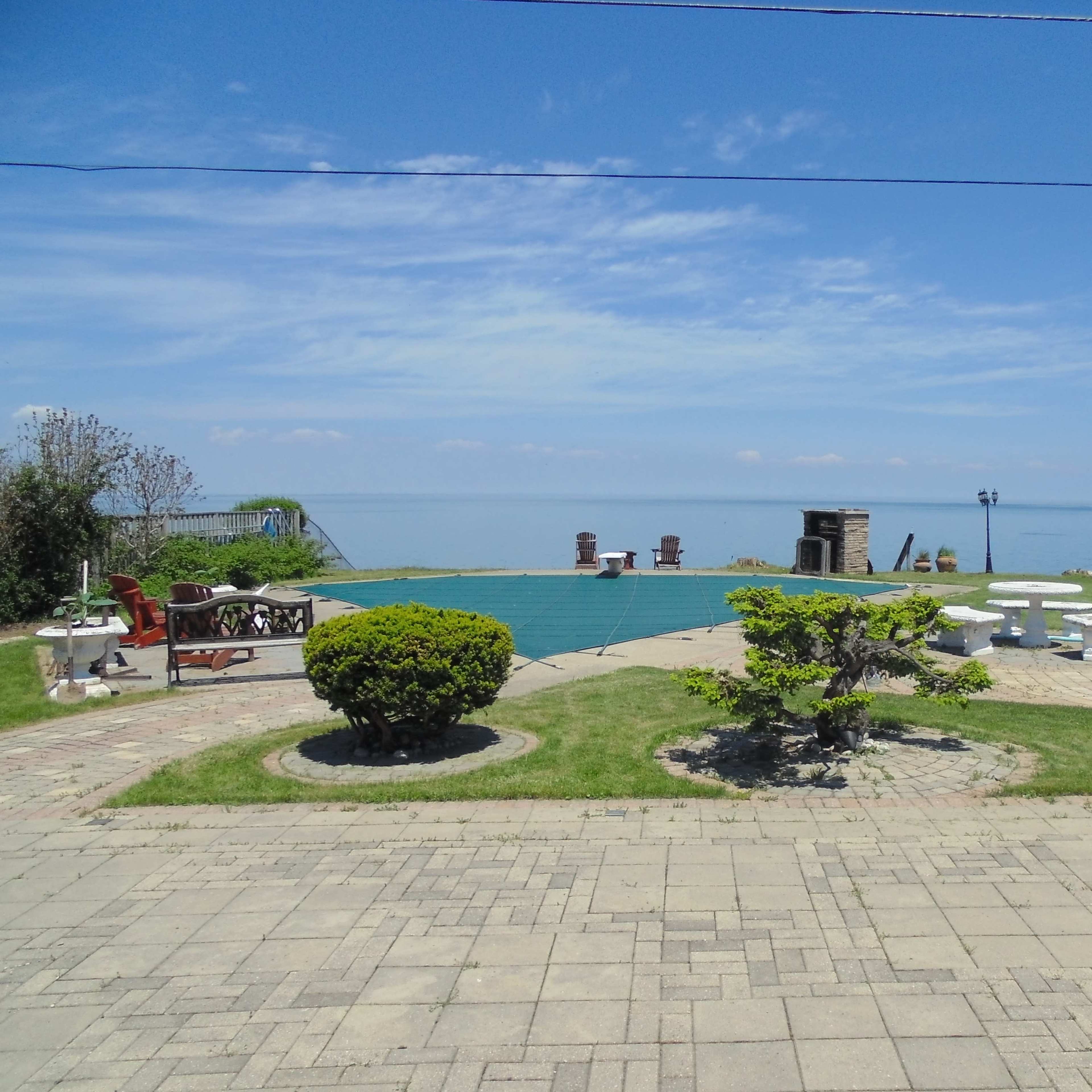 A well-maintained patio with seating areas overlooks a calm body of water under a clear sky.