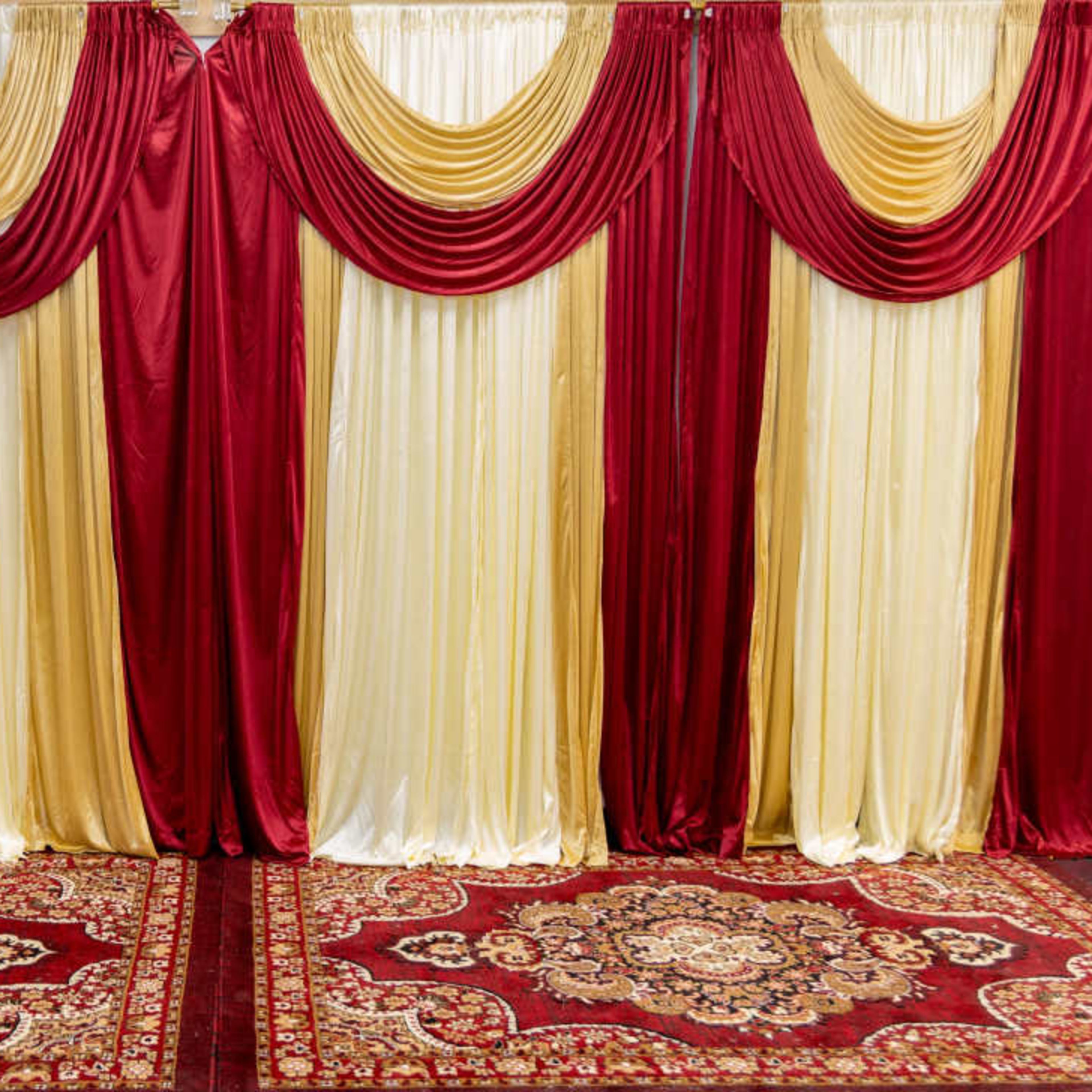 A decorative backdrop with red and gold draped fabric and a patterned carpet in a similar color scheme.