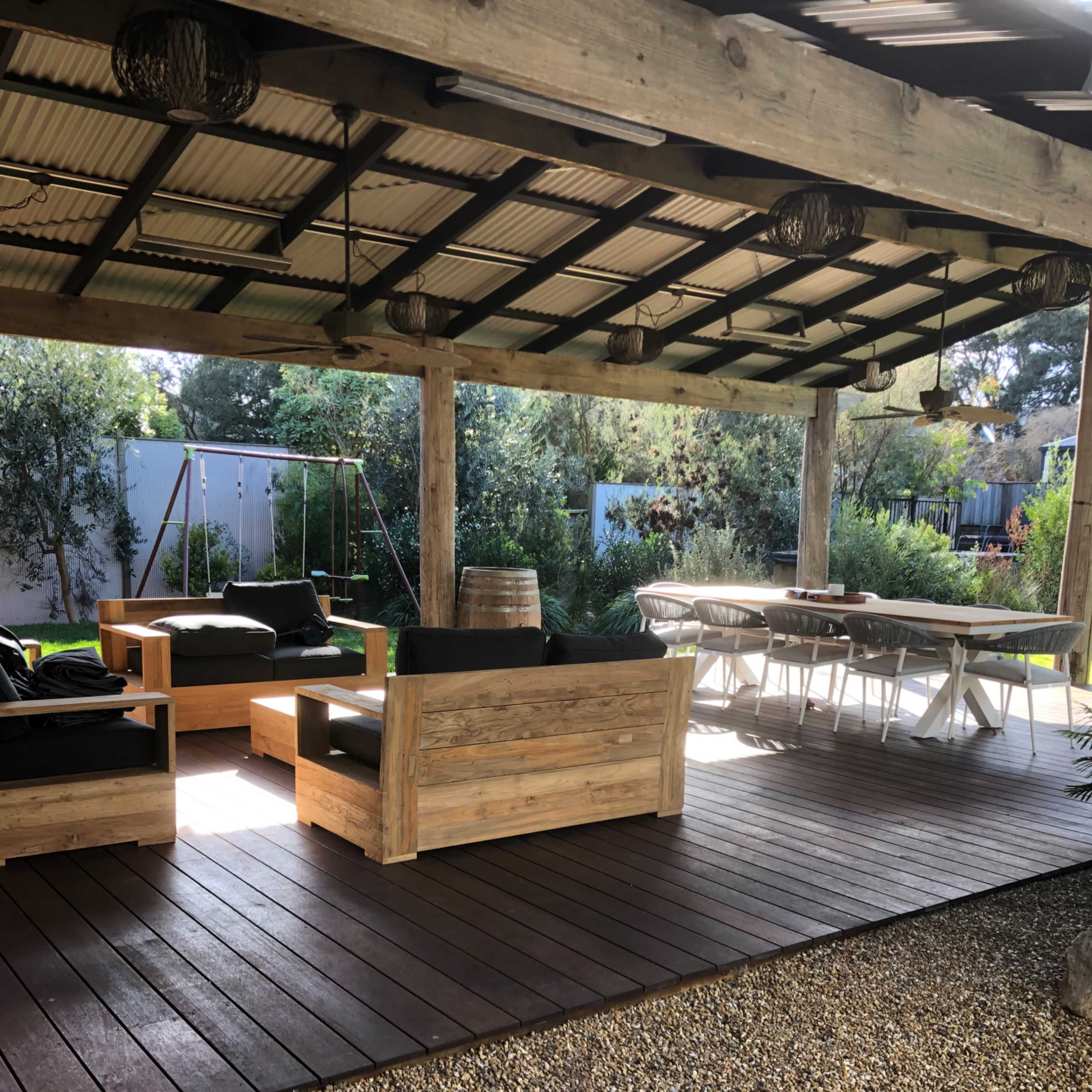 A shaded outdoor seating area with wooden furniture, a gravel floor, and a dining table under a roofed patio.