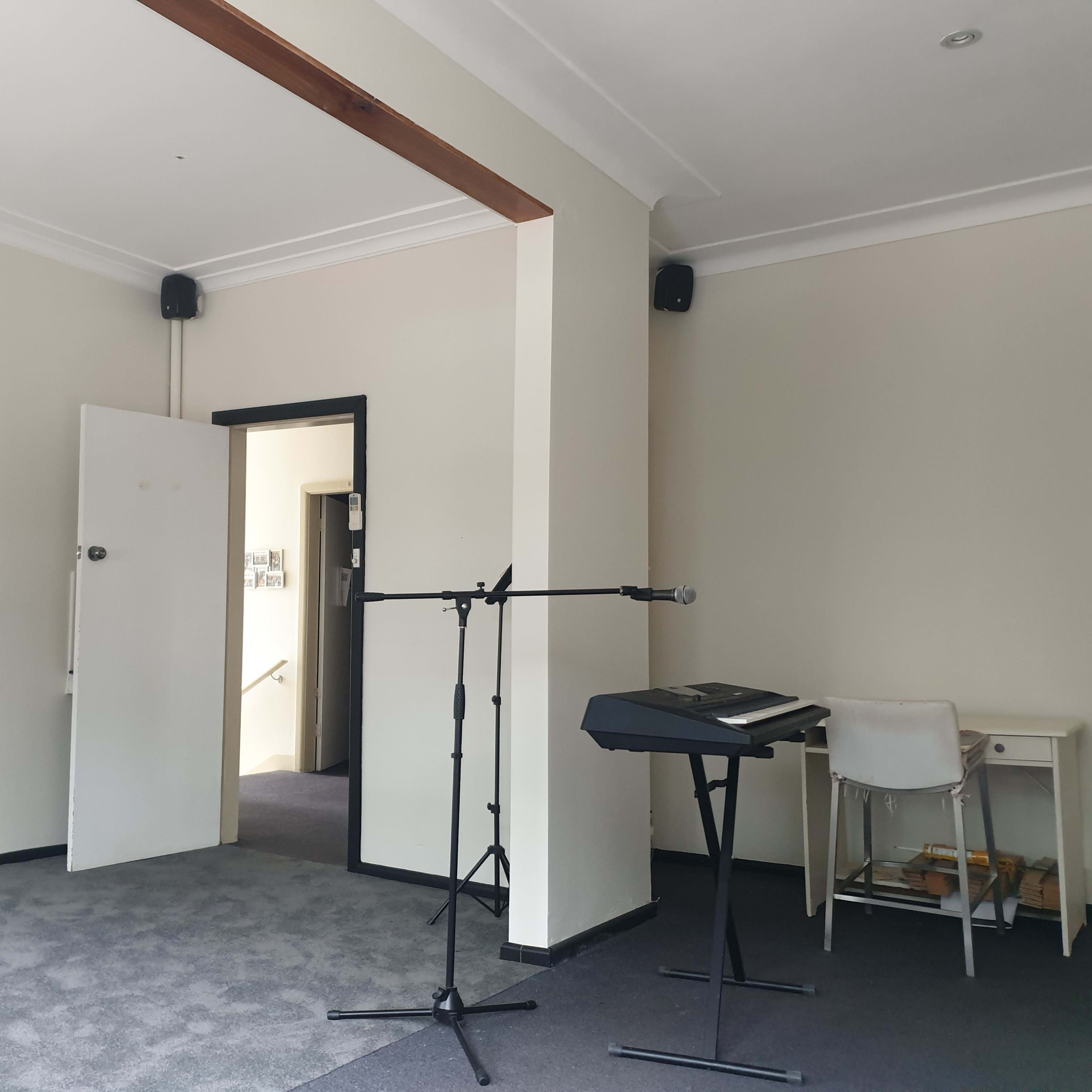 A small room features a doorway, a keyboard on a stand, a microphone, and a whiteboard mounted on the wall.