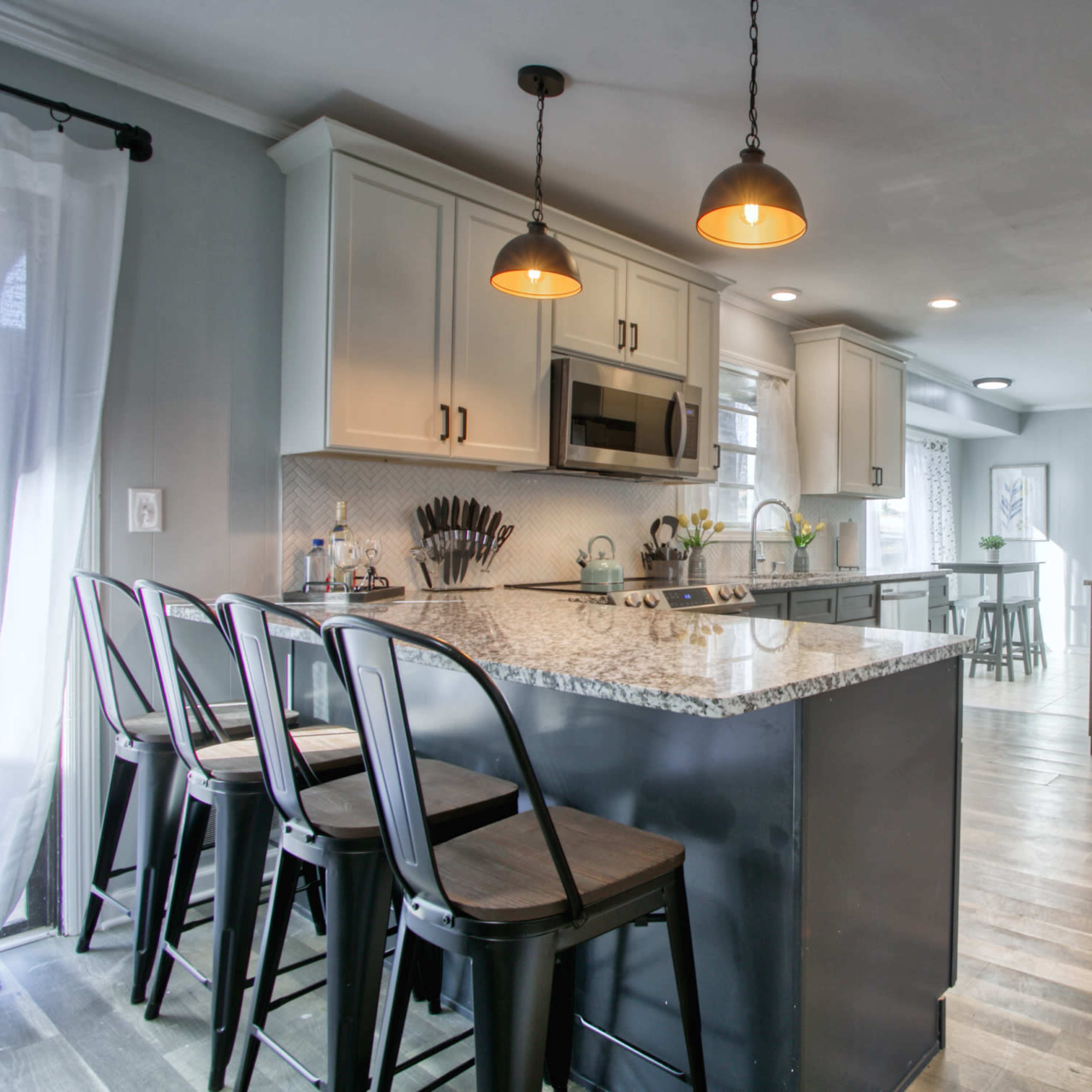 A modern kitchen featuring a central island with bar stools, stainless steel appliances, and light-colored cabinetry.