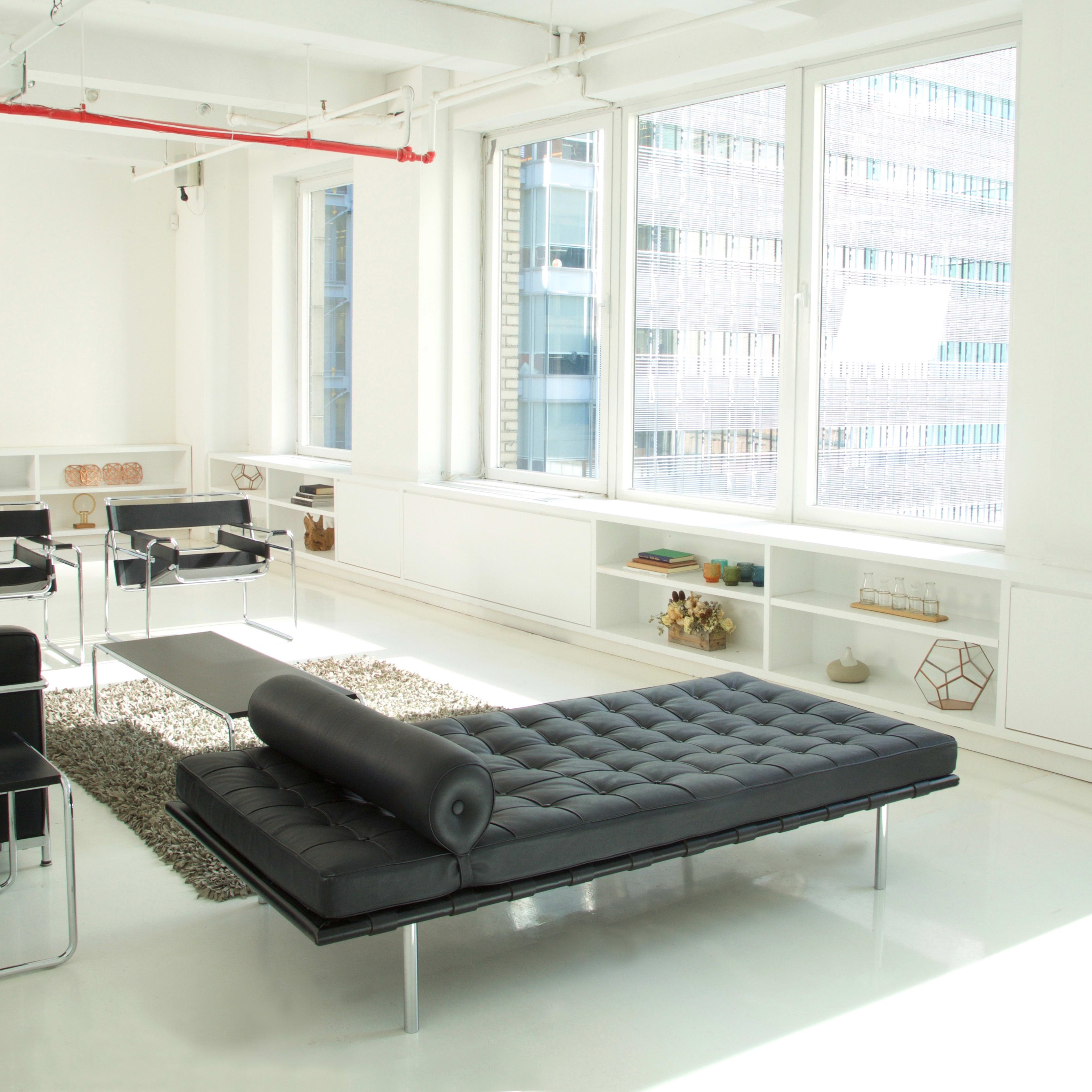A modern, minimalist living space with large windows, a black sofa, and sleek furniture arrangements on a polished white floor.