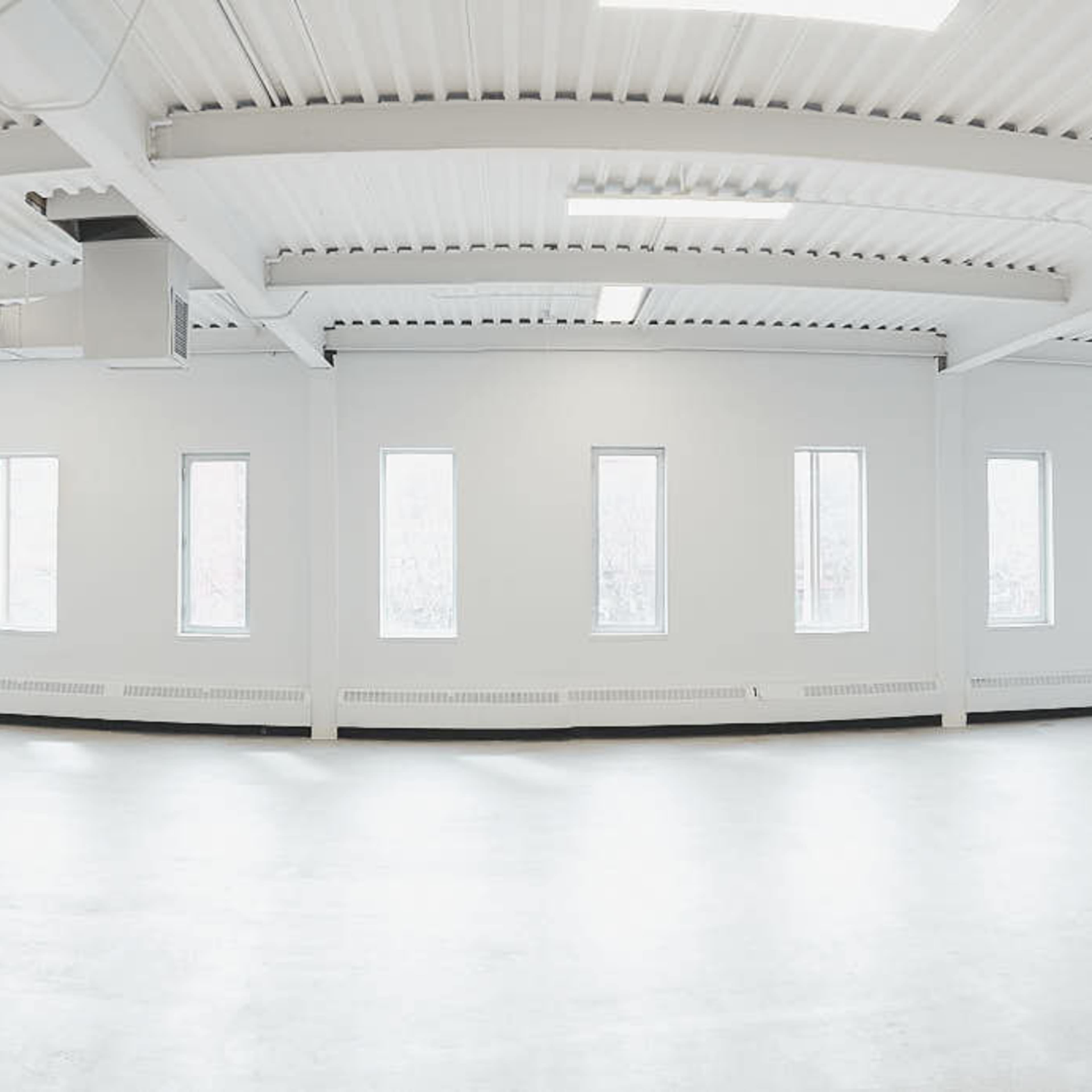 A large, empty room with white walls, several windows, and a smooth concrete floor.