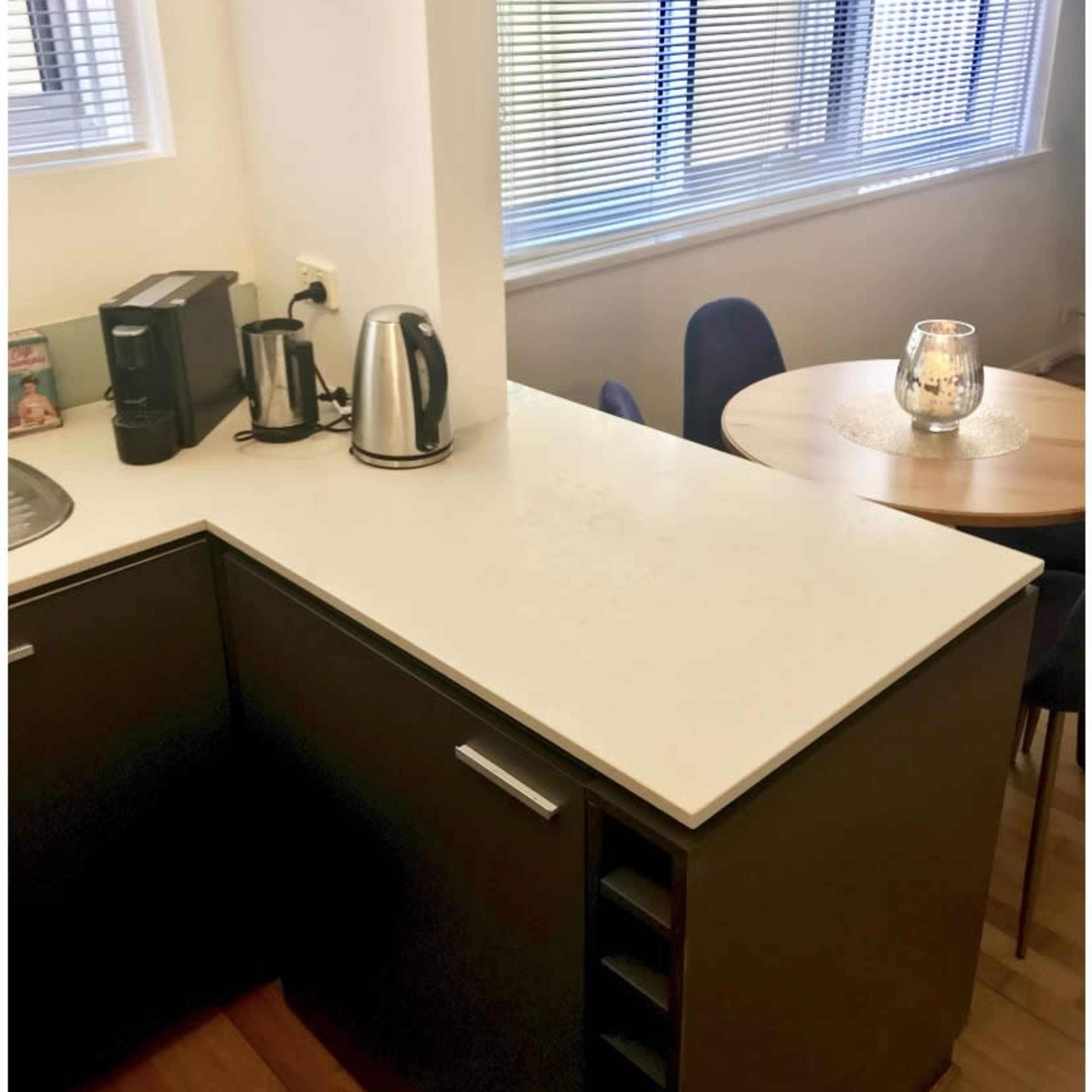A kitchen corner with a coffee maker and kettle on a countertop, alongside a dining area featuring a round table and chairs.