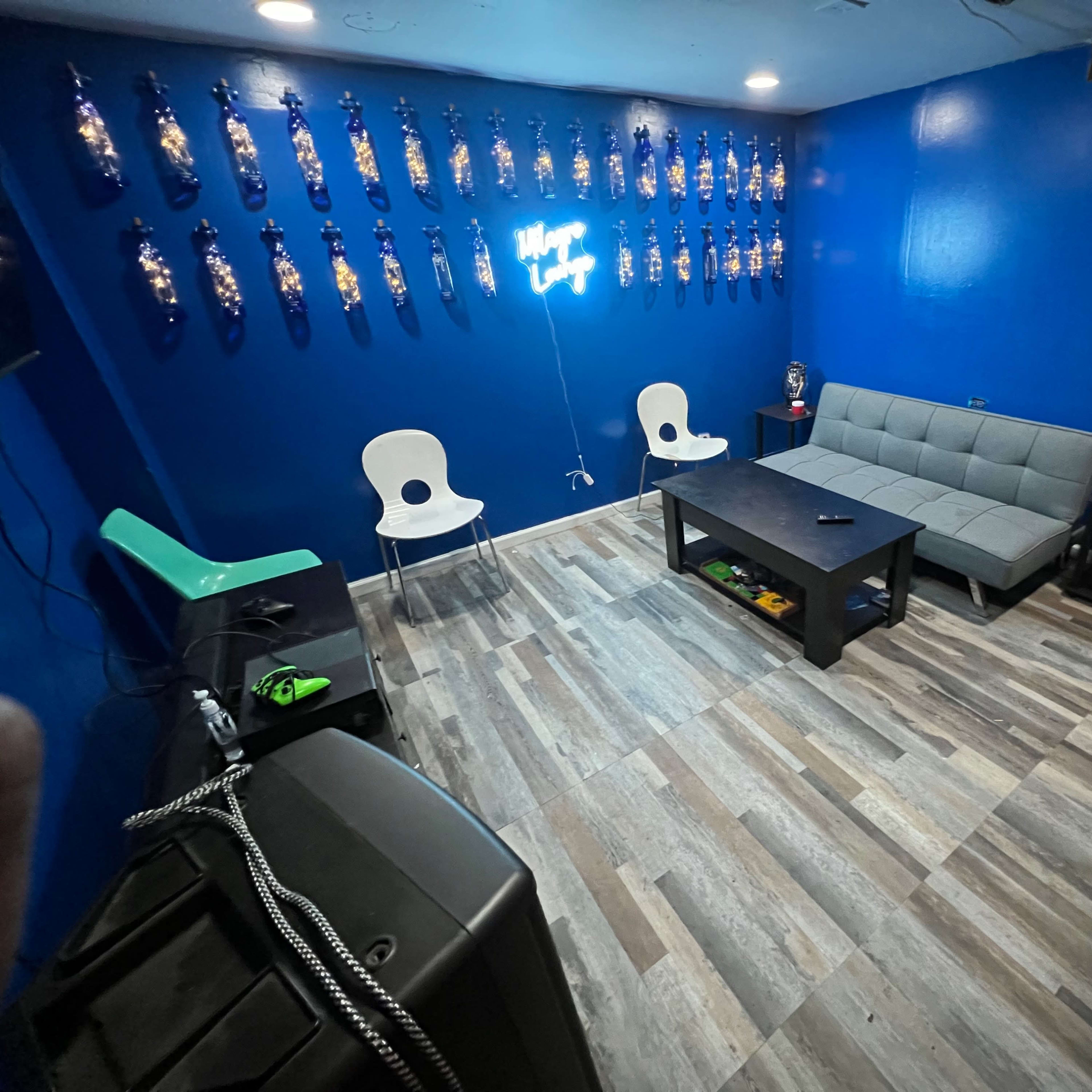 The room features a blue wall adorned with decorative bottles, a gray sofa, two white chairs, and a dark coffee table on a wood-patterned floor.